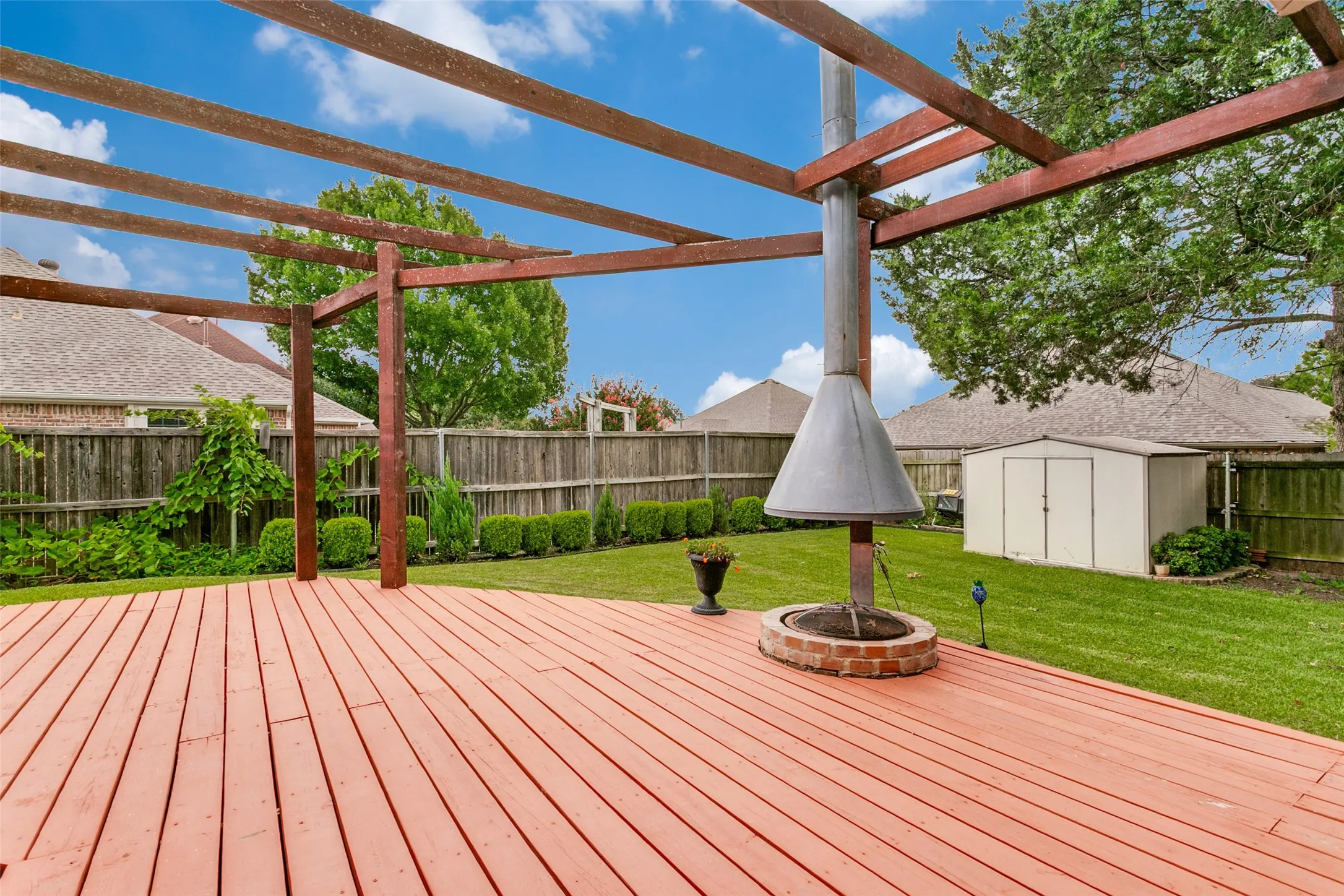 Spacious wooden deck featuring an overhead pergola structure and a built-in outdoor fireplace