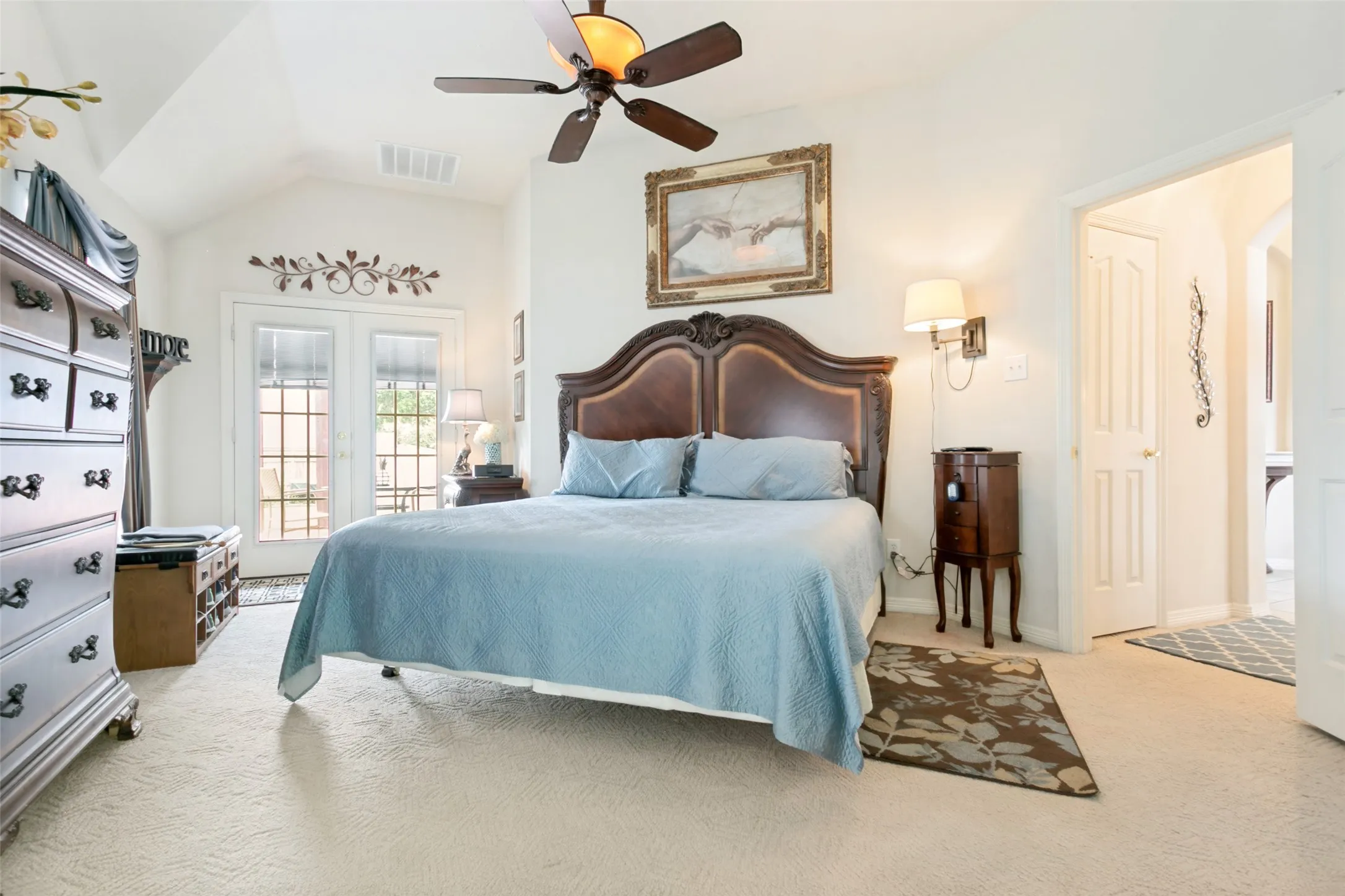 Vaulted ceiling bedroom with light-toned carpeting and direct outdoor access via double doors