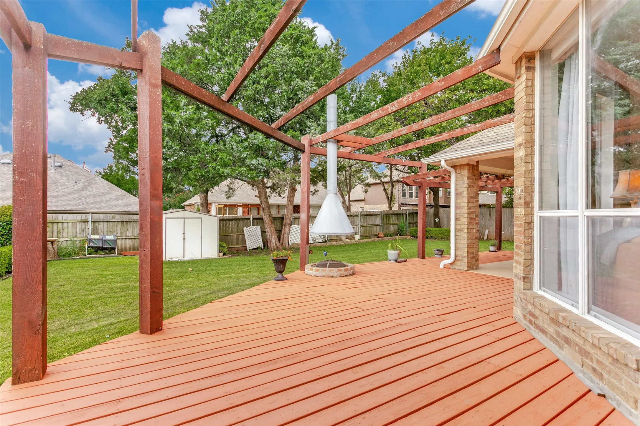 Expansive wood deck with an overhead pergola, brick exterior accent, and a built-in outdoor fireplace feature