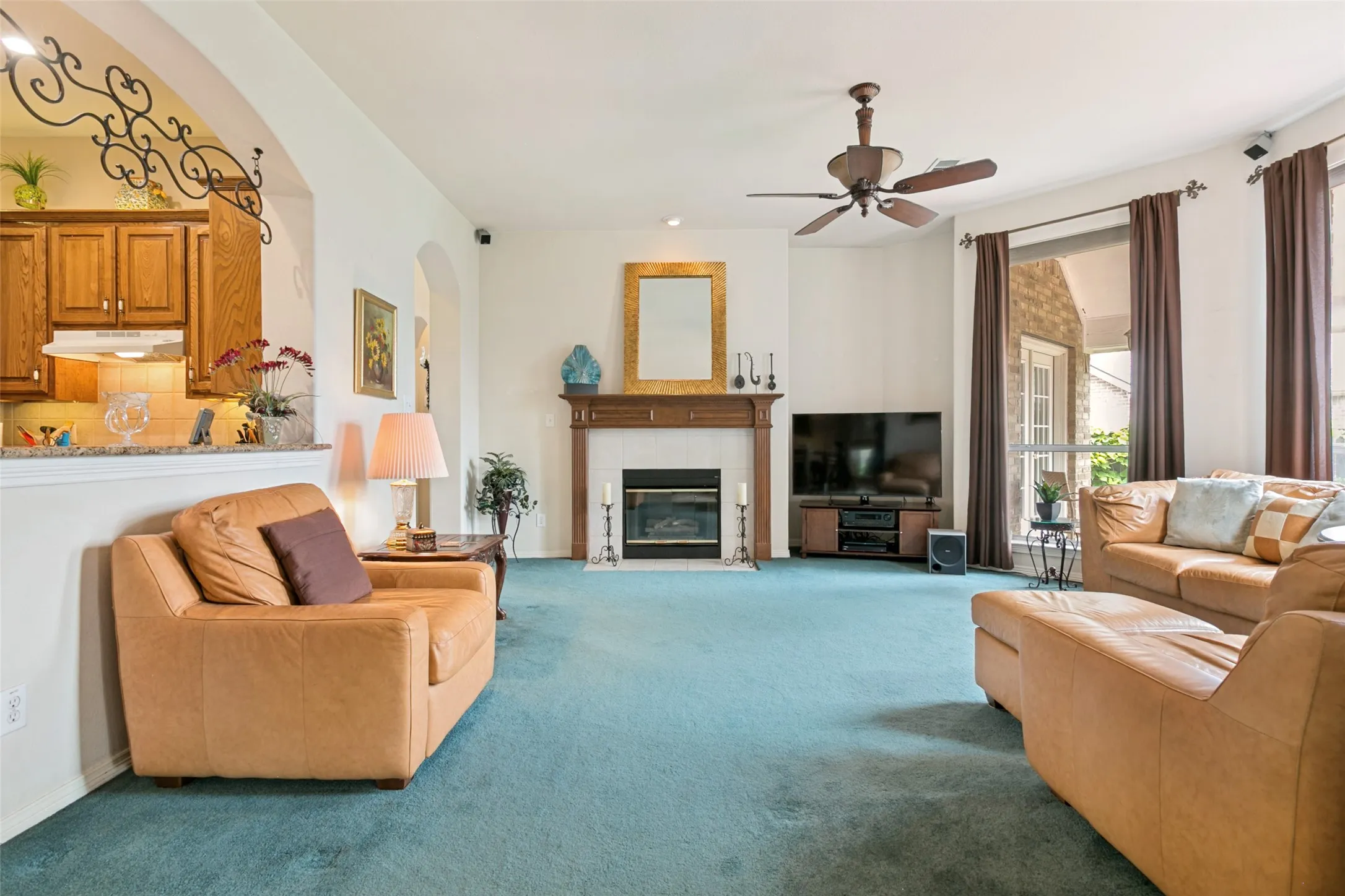 Living area featuring a fireplace with a wood mantel, a ceiling fan, and large windows with privacy drapes