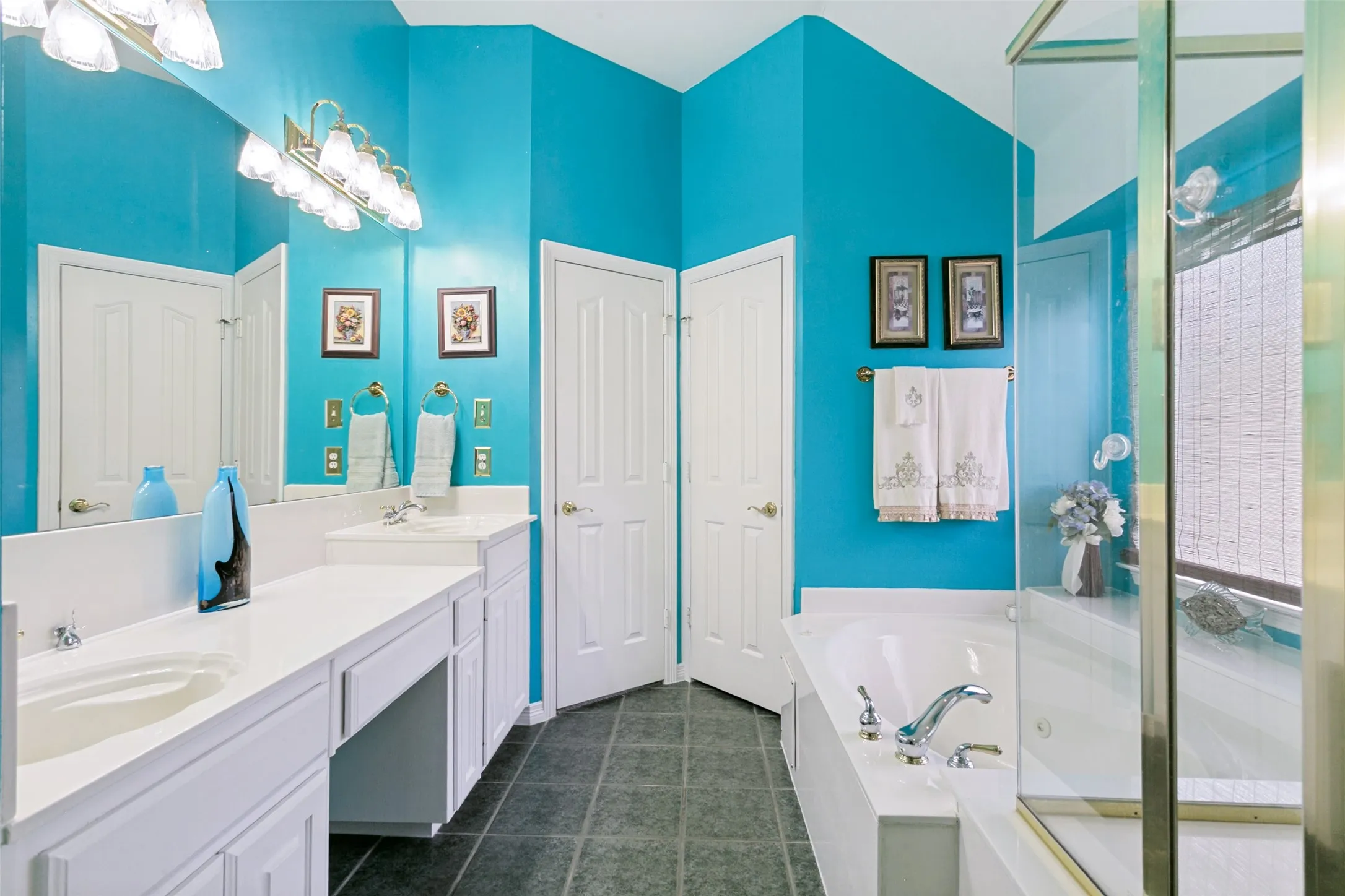 Bathroom featuring dual basin vanity with white cabinetry, built-in soaking tub with chrome fixtures, and a separate glass-enclosed shower