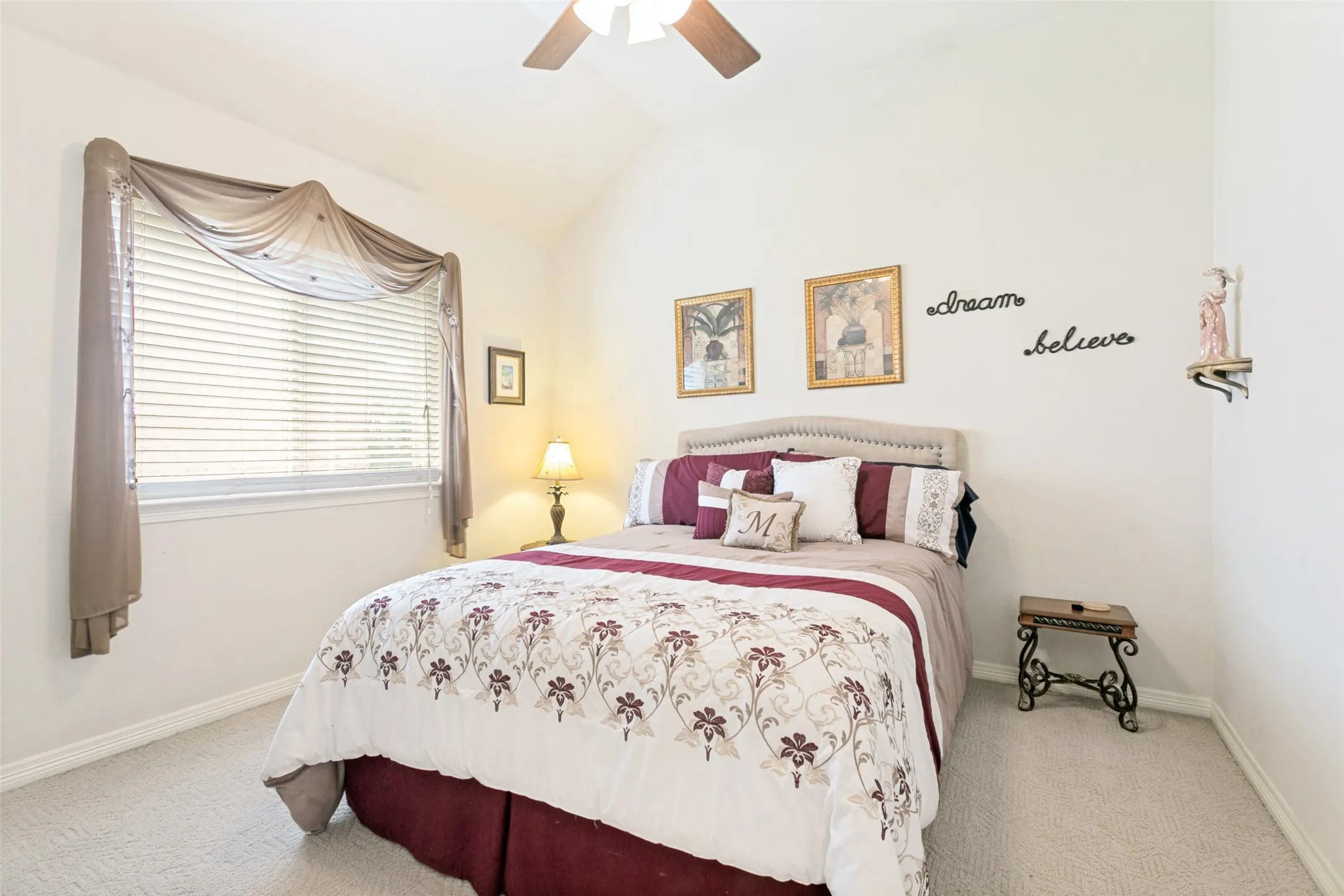 Carpeted room featuring a vaulted ceiling with a ceiling fan, a window with horizontal blinds, and a padded headboard