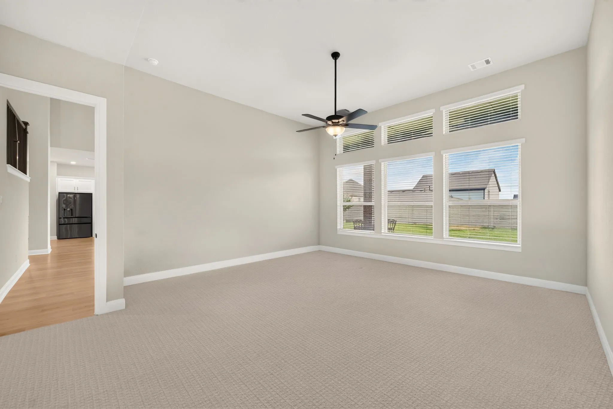 Spacious room featuring neutral carpeting, a ceiling fan, and a wall of windows including transom windows