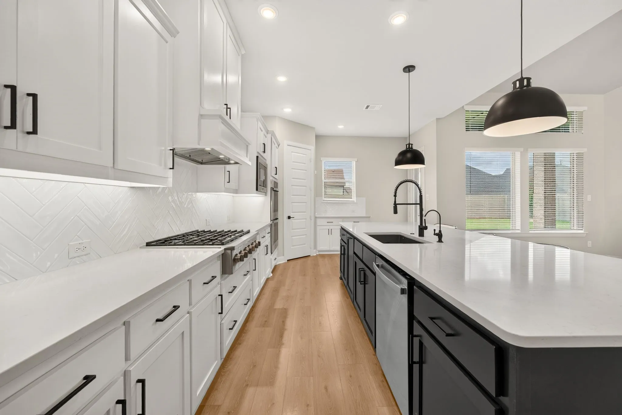 Gourmet kitchen featuring white shaker cabinetry, an expansive central island with a sink, a gas range with a custom vent hood, and light wood-finish flooring