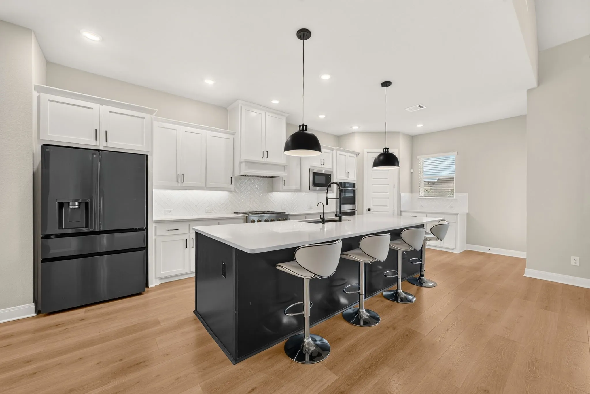 Modern kitchen featuring a large island with seating, white shaker cabinetry, white subway tile backsplash, and wood-finish flooring