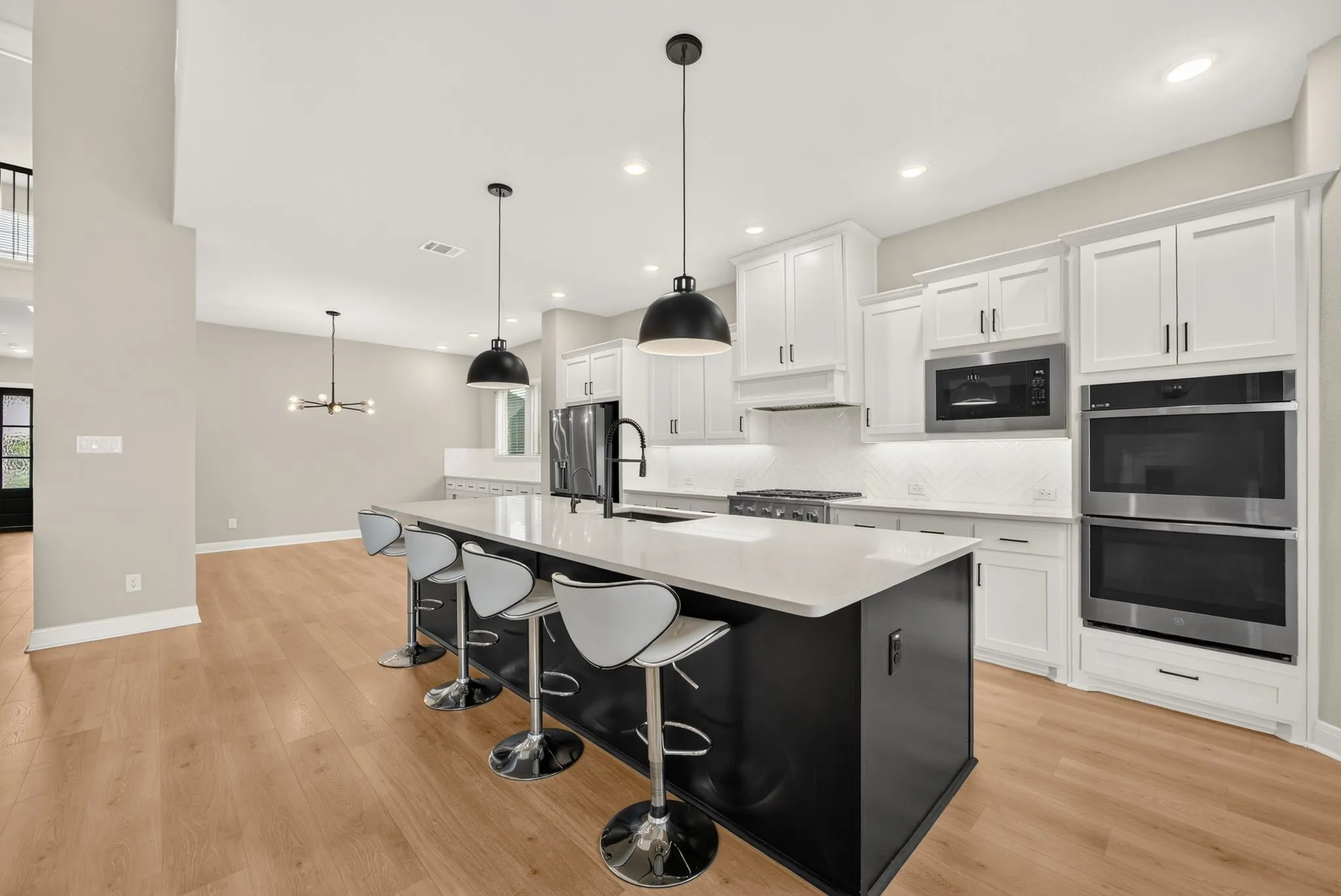 Spacious kitchen featuring a large island with white countertop, white upper and lower cabinetry, stainless steel appliances, and wood-finish flooring