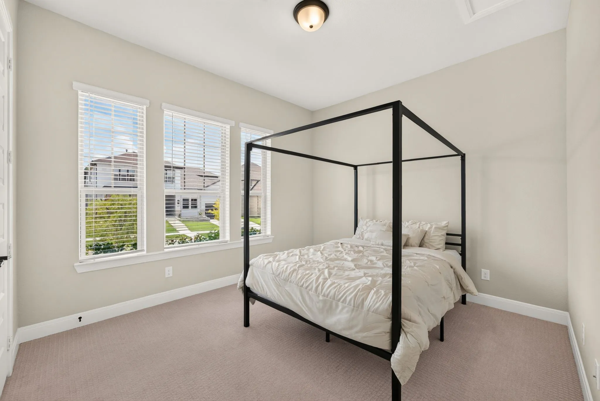 Neutral-toned room featuring three large windows with blinds, carpeted flooring, a ceiling-mounted light fixture, and white baseboards