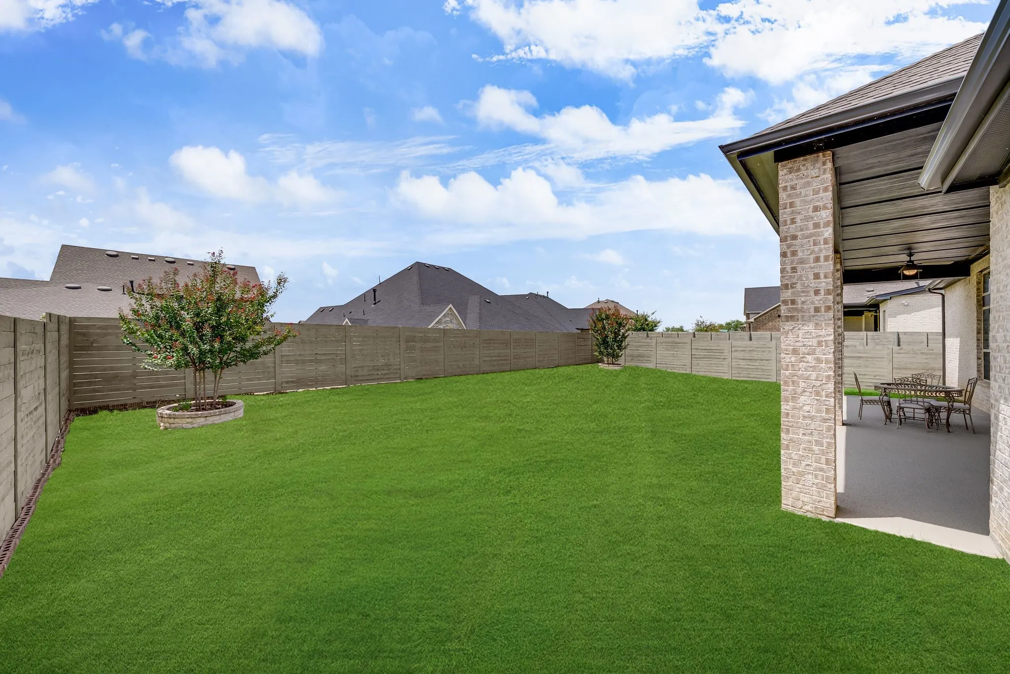 Expansive green lawn framed by a privacy fence, featuring a covered patio with a ceiling fan and recessed lighting