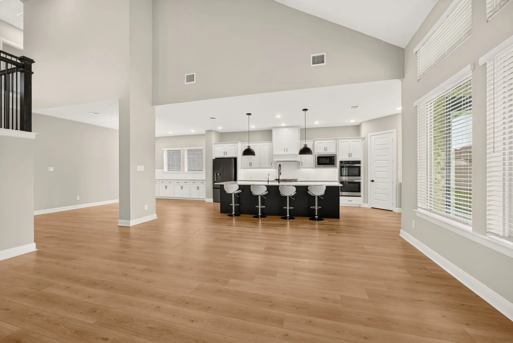 Open-concept living space featuring vaulted ceilings, wood-finish flooring, a modern kitchen island with seating, pendant lighting, and multiple windows with blinds