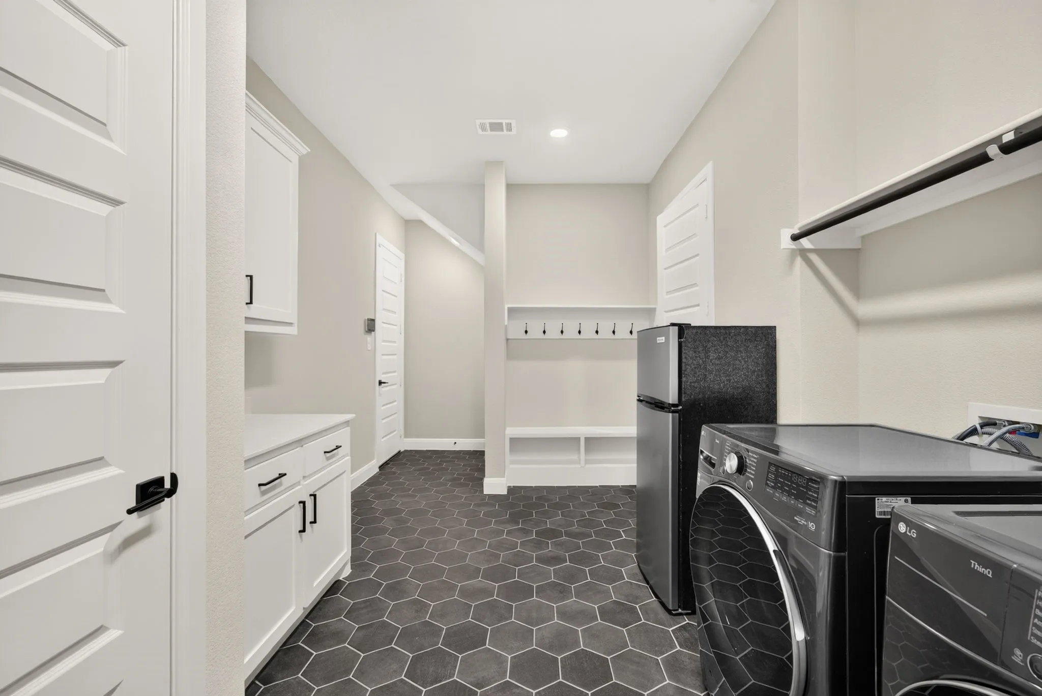 Spacious utility room featuring hexagonal tile flooring, white cabinetry with black hardware, built-in shelving, a hanging rod, and recessed lighting