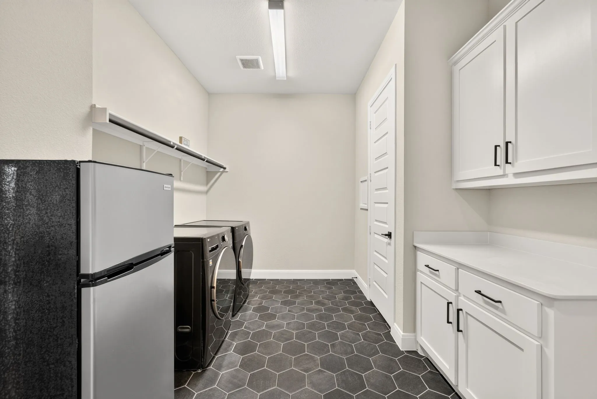 Laundry room featuring hexagonal floor tiling, white cabinetry with dark hardware, white countertops, and a full-size refrigerator