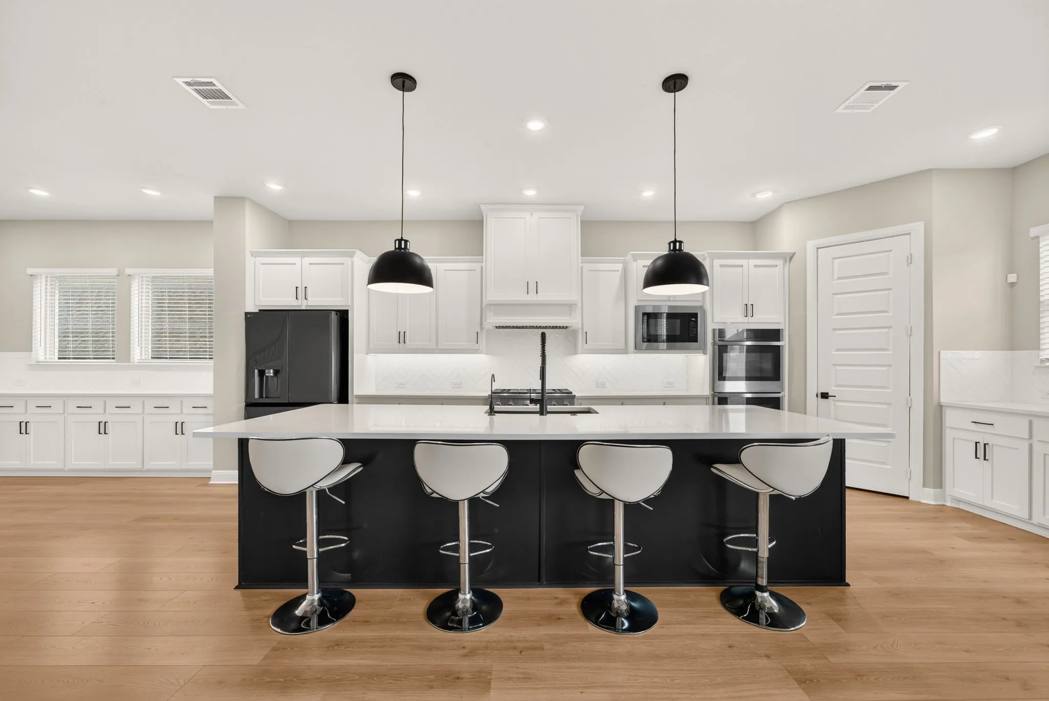 Spacious kitchen featuring a large island with seating, white shaker cabinetry, stainless steel appliances, and wood-finish flooring