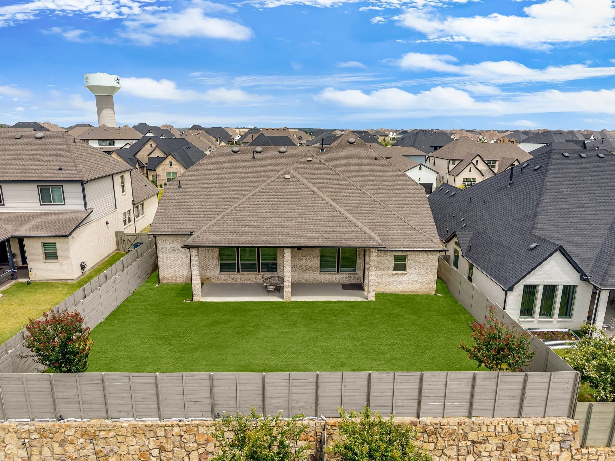 Expansive fenced backyard featuring a manicured lawn, a covered concrete patio, and mature landscaping