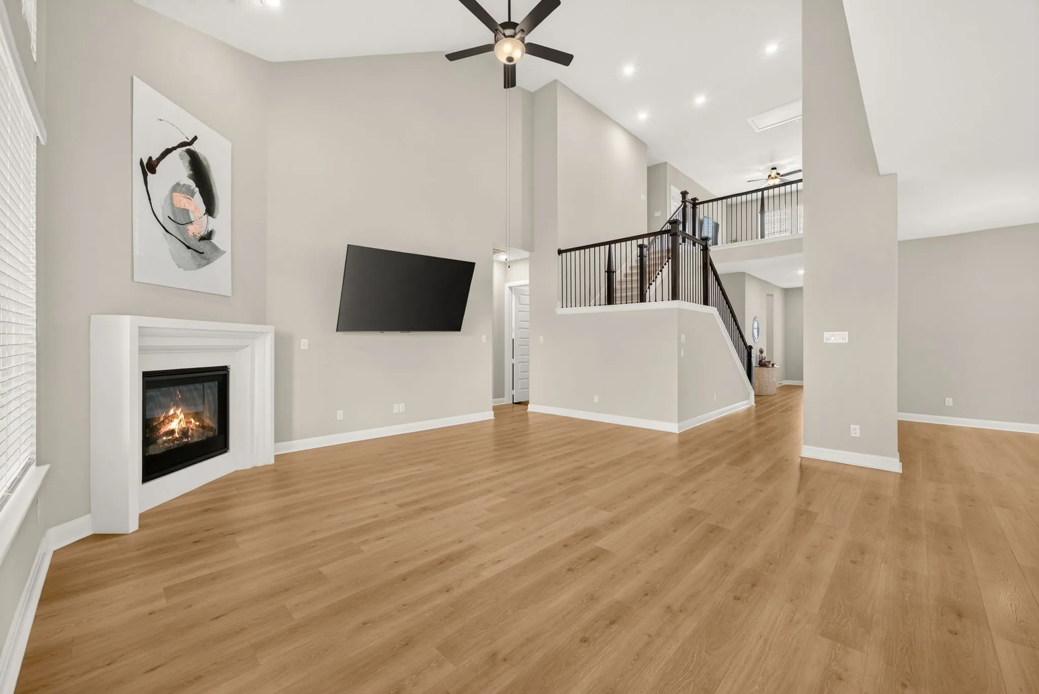 Two-story living area featuring a corner fireplace with white mantel, wood-finish flooring, a ceiling fan, and recessed lighting