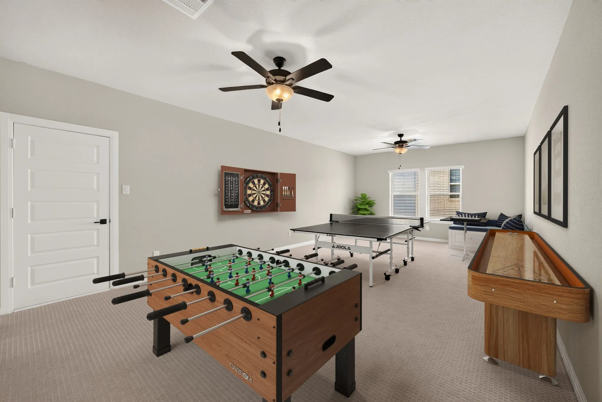 Spacious recreation room featuring neutral wall tones, carpet flooring, dual ceiling fans with integrated lighting, and multiple windows with blinds