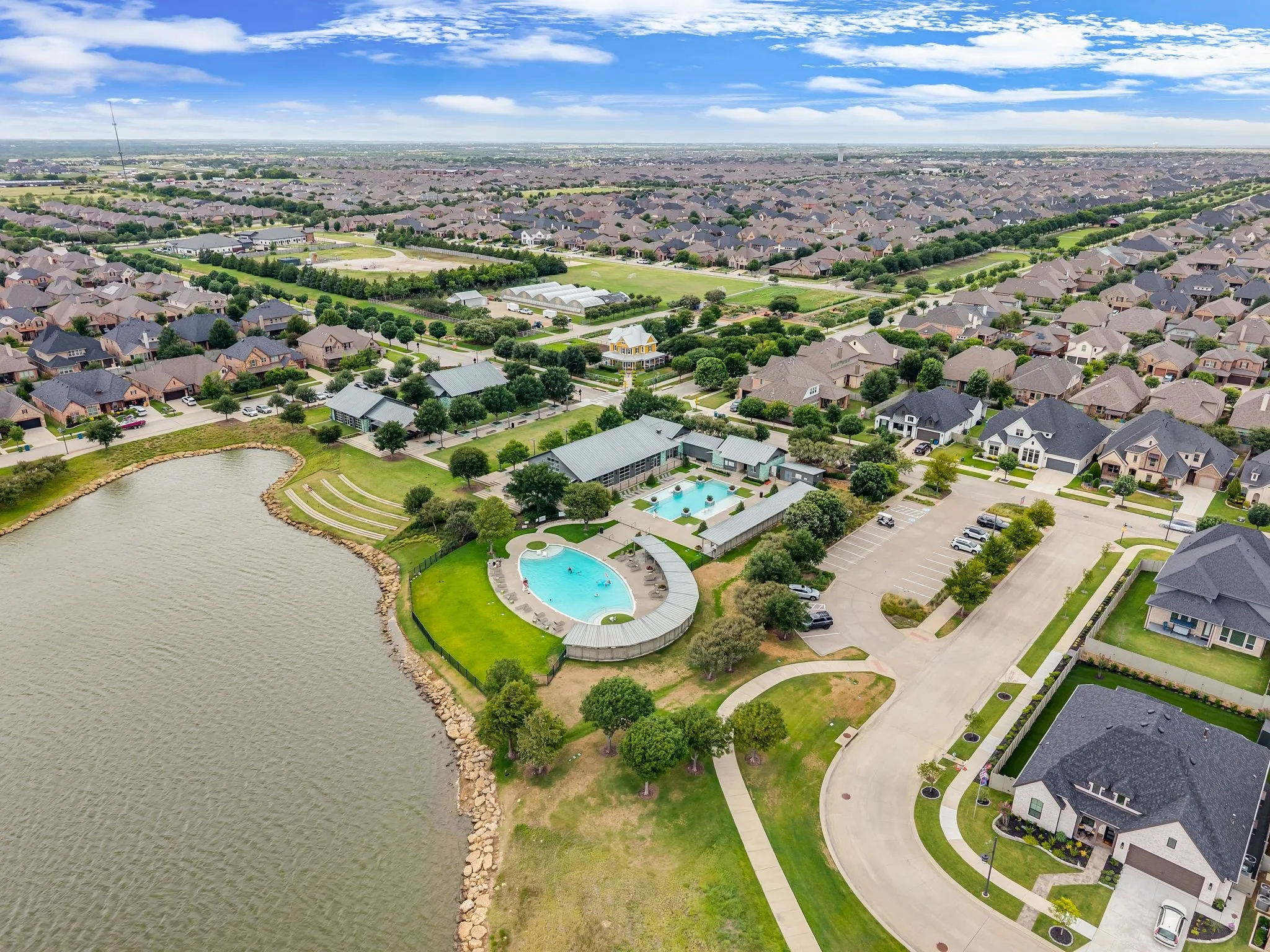 Aerial perspective showcasing a residential community with a large body of water, a central amenity complex, and surrounding homes