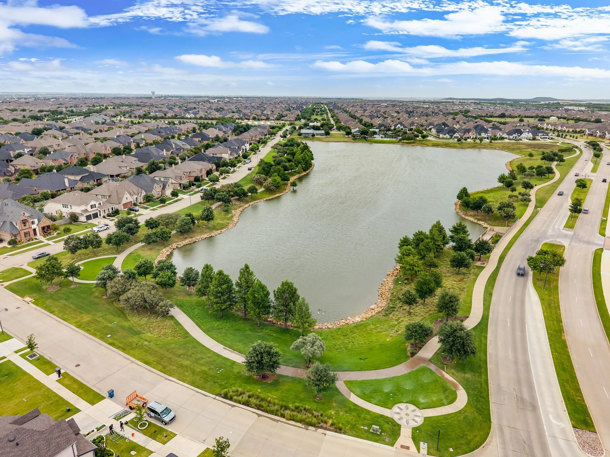 Expansive community lake with surrounding parkland, walking paths, and mature trees, bordered by residential streets and single-family homes