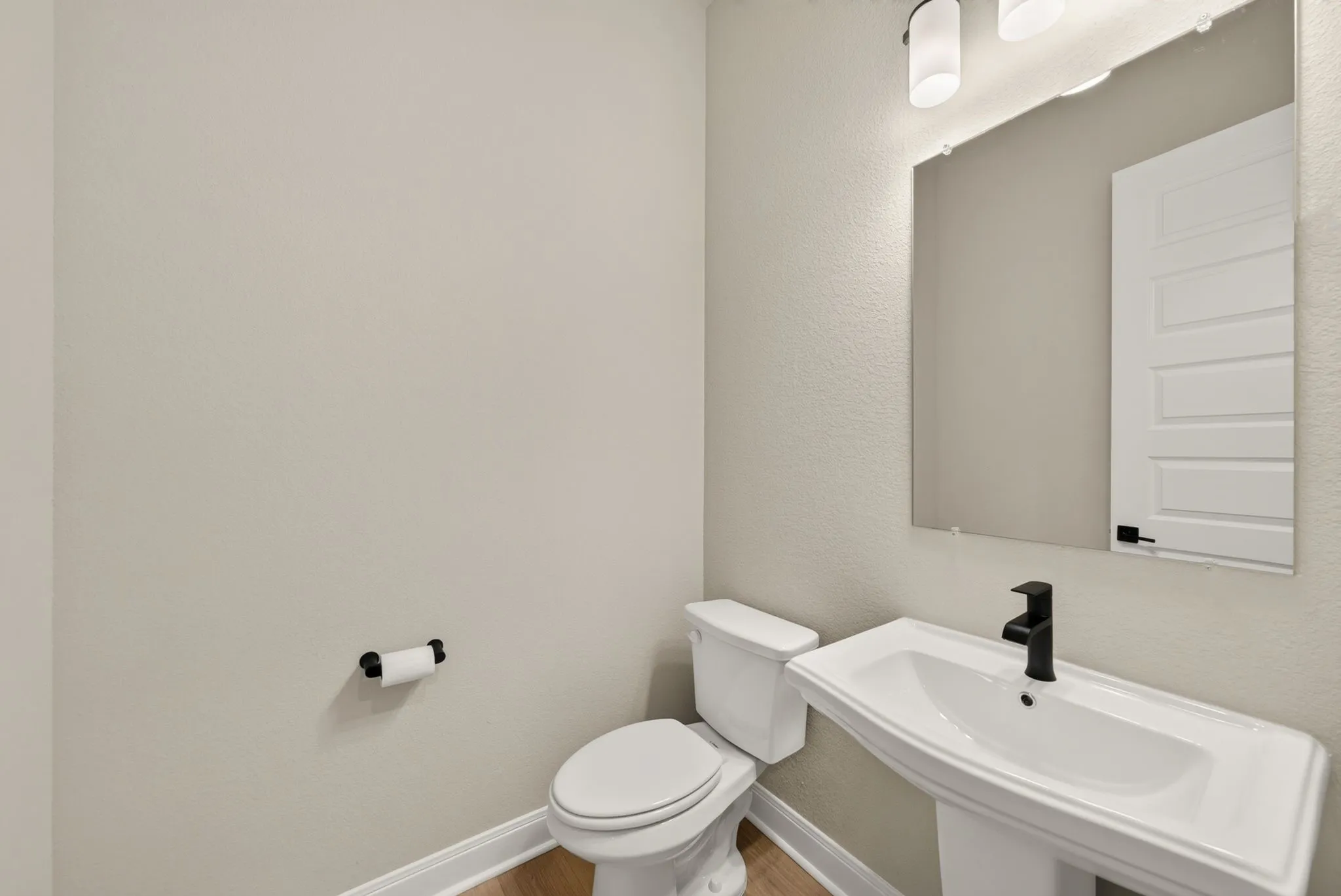 Pedestal sink with matte black faucet, framed mirror, and two-light vanity fixture