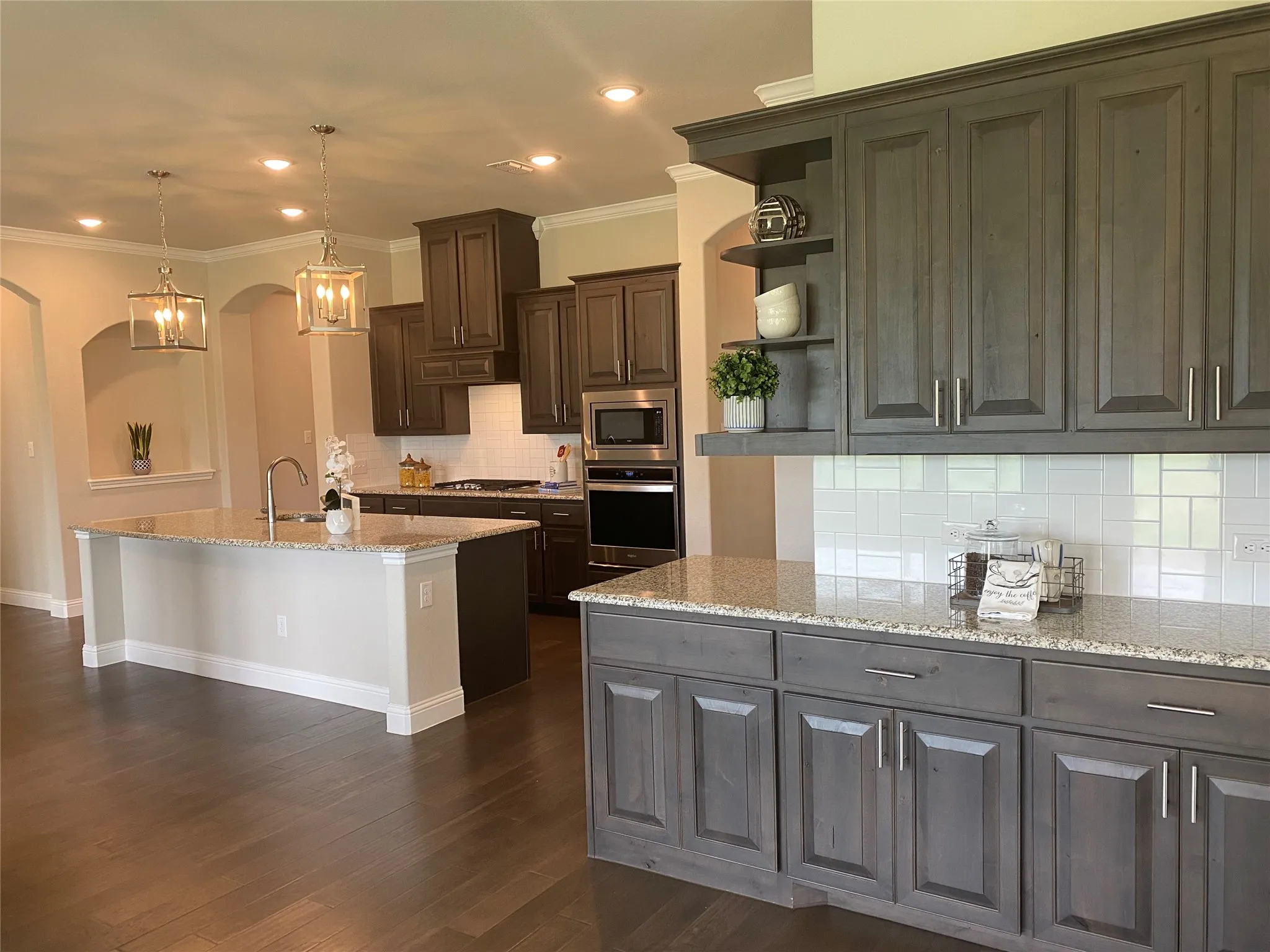 Kitchen with appliances with stainless steel finishes, tasteful backsplash, a kitchen island with sink, light stone countertops, and dark hardwood / wood-style flooring