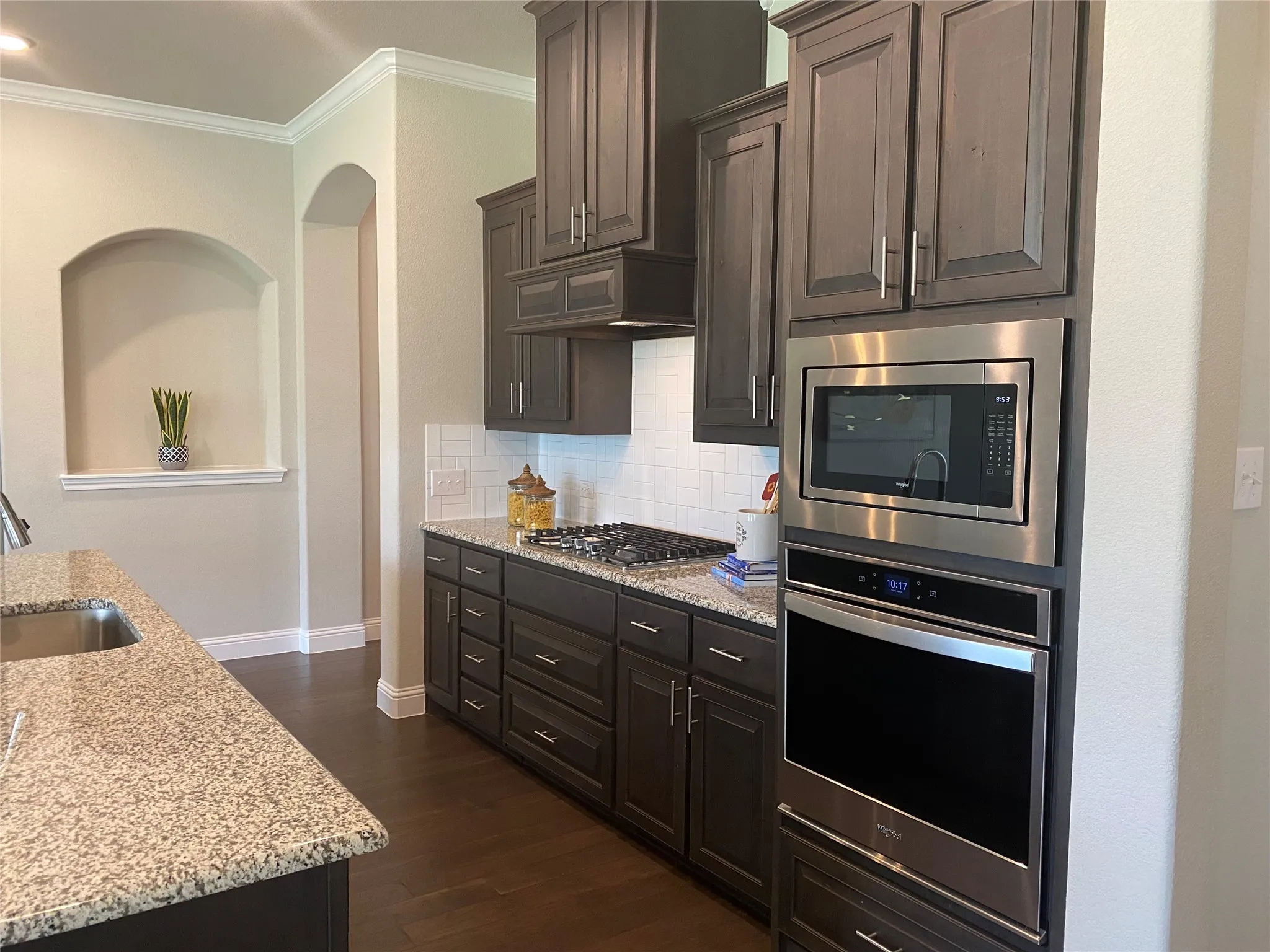 Kitchen featuring tasteful backsplash, dark wood-type flooring, light stone counters, appliances with stainless steel finishes, and sink