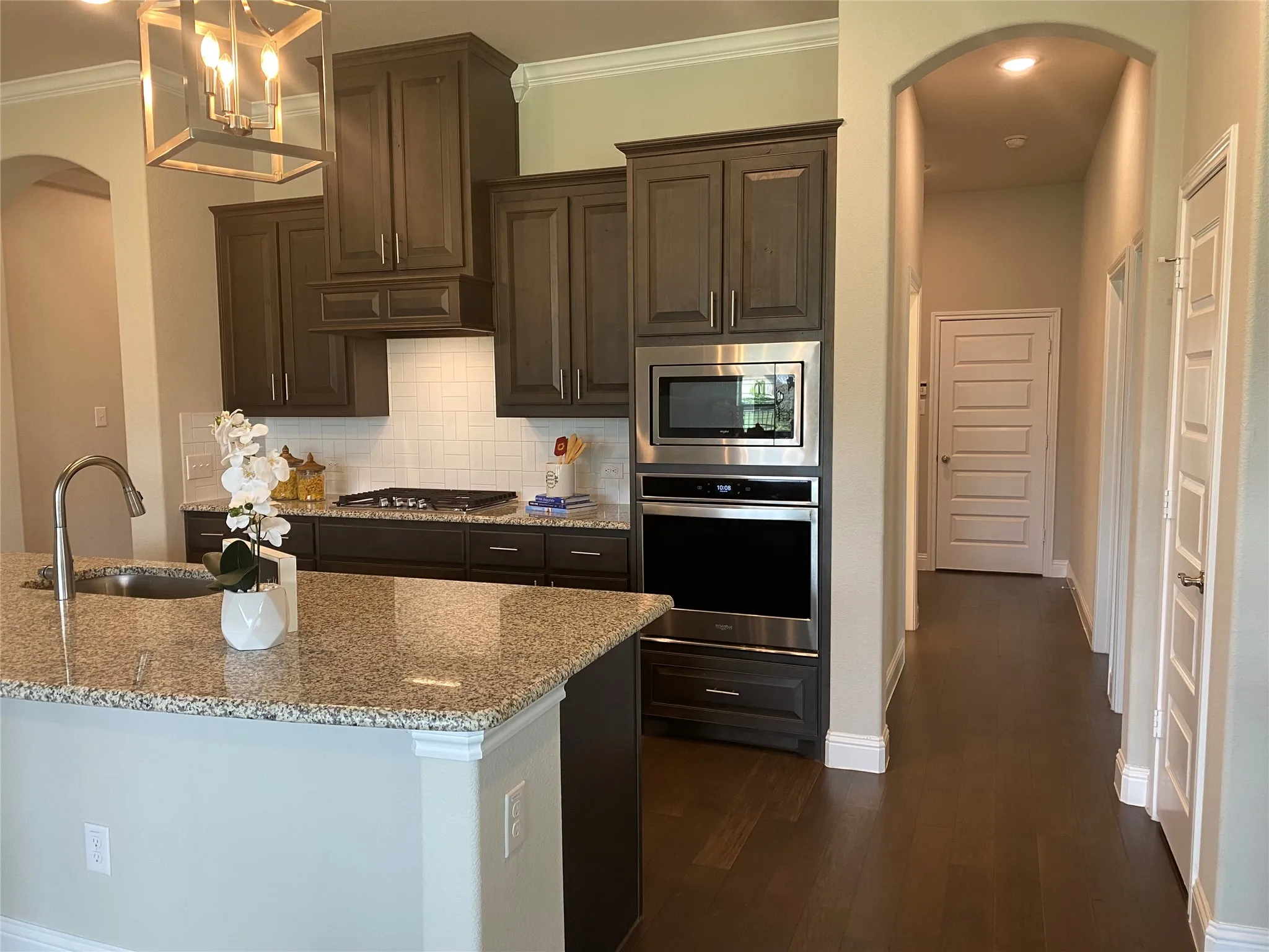 Kitchen featuring crown molding, dark wood-type flooring, light stone counters, appliances with stainless steel finishes, and decorative backsplash