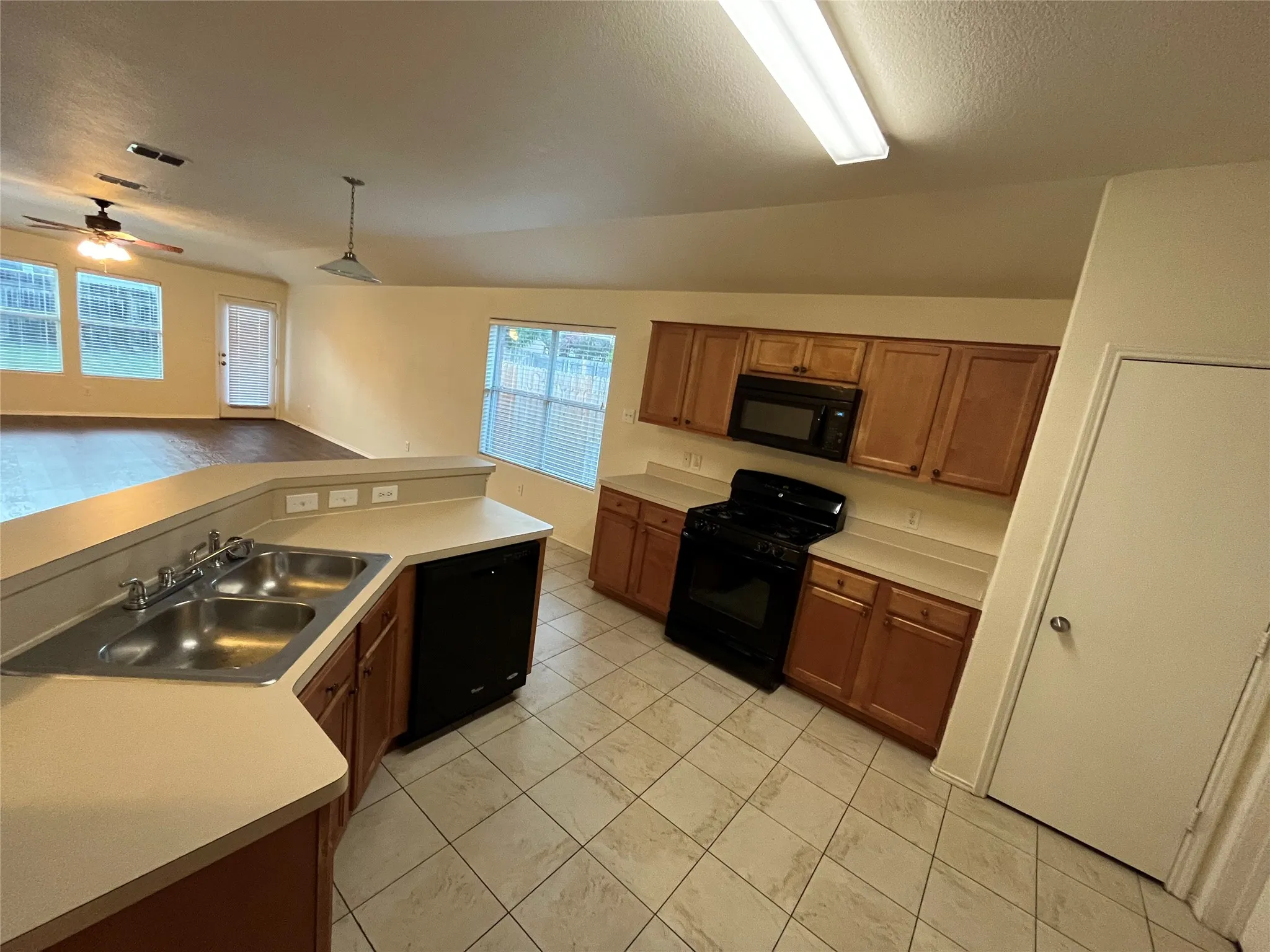 Kitchen featuring tile flooring, light wood-finish cabinetry, solid surface countertops, a double basin stainless steel sink, and black appliances