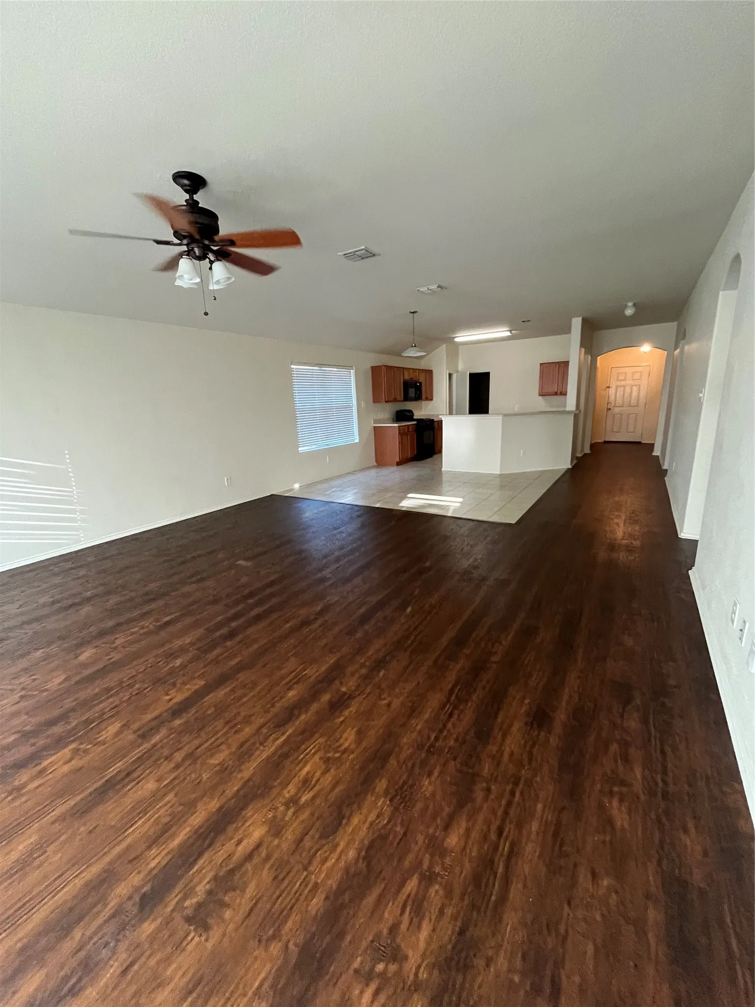 Open-concept living area featuring wood-finish flooring, a ceiling fan with integrated lighting, and a light-toned kitchen with wood cabinetry and a breakfast bar