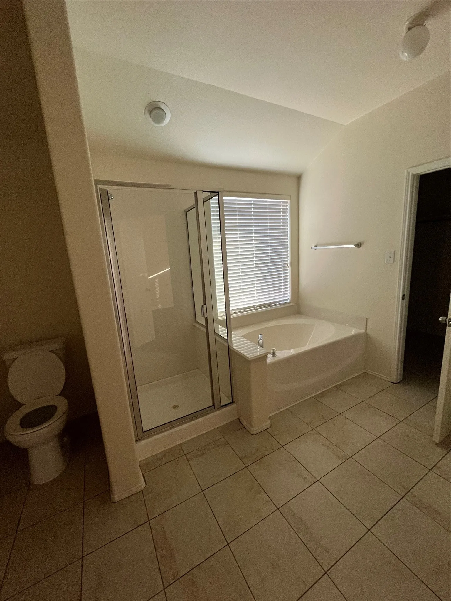 Bathroom featuring a glass-enclosed shower, a built-in soaking tub under a window, and neutral tile flooring