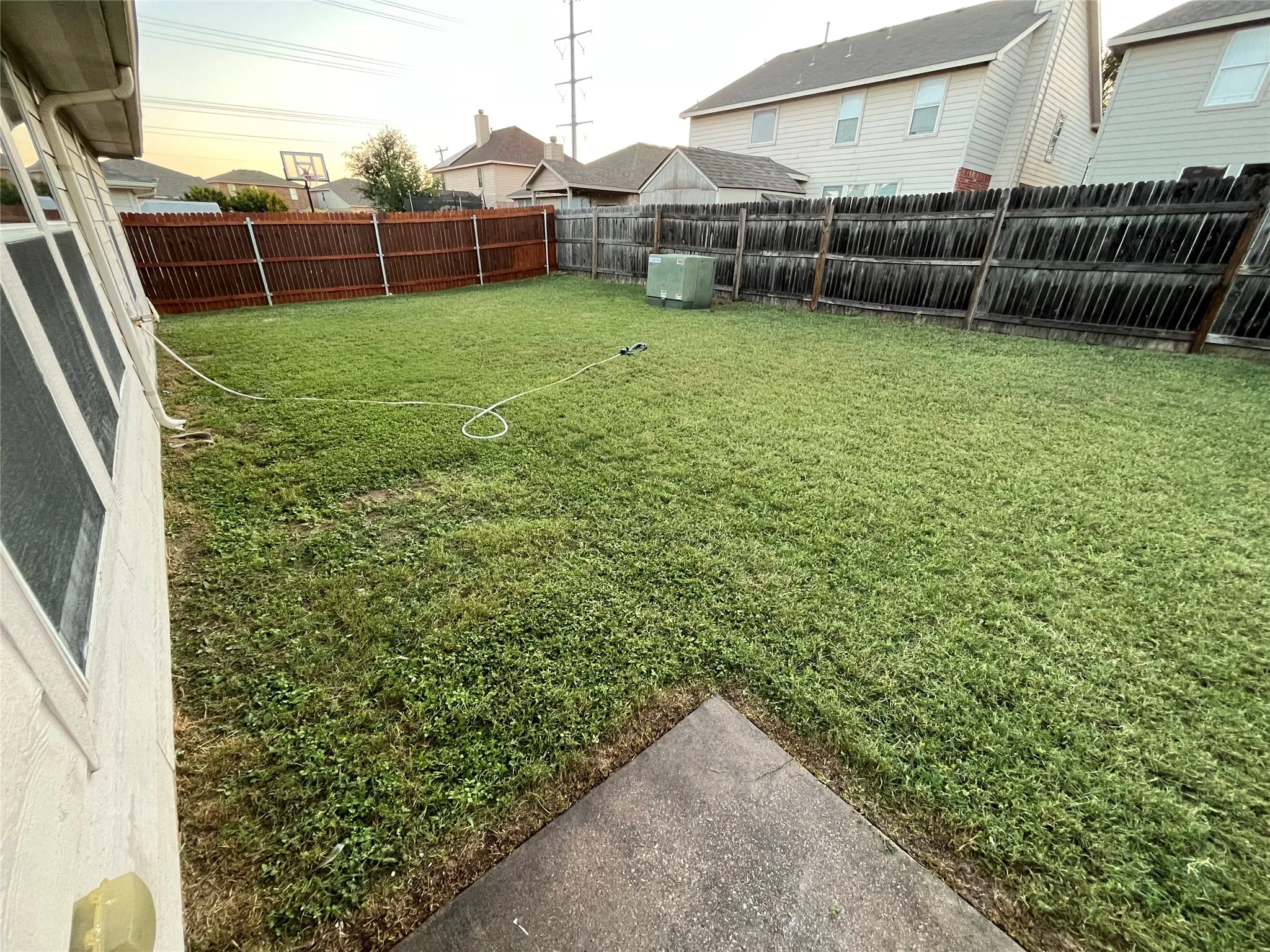 Expansive backyard featuring a large grass lawn, wood privacy fencing, and a concrete patio space