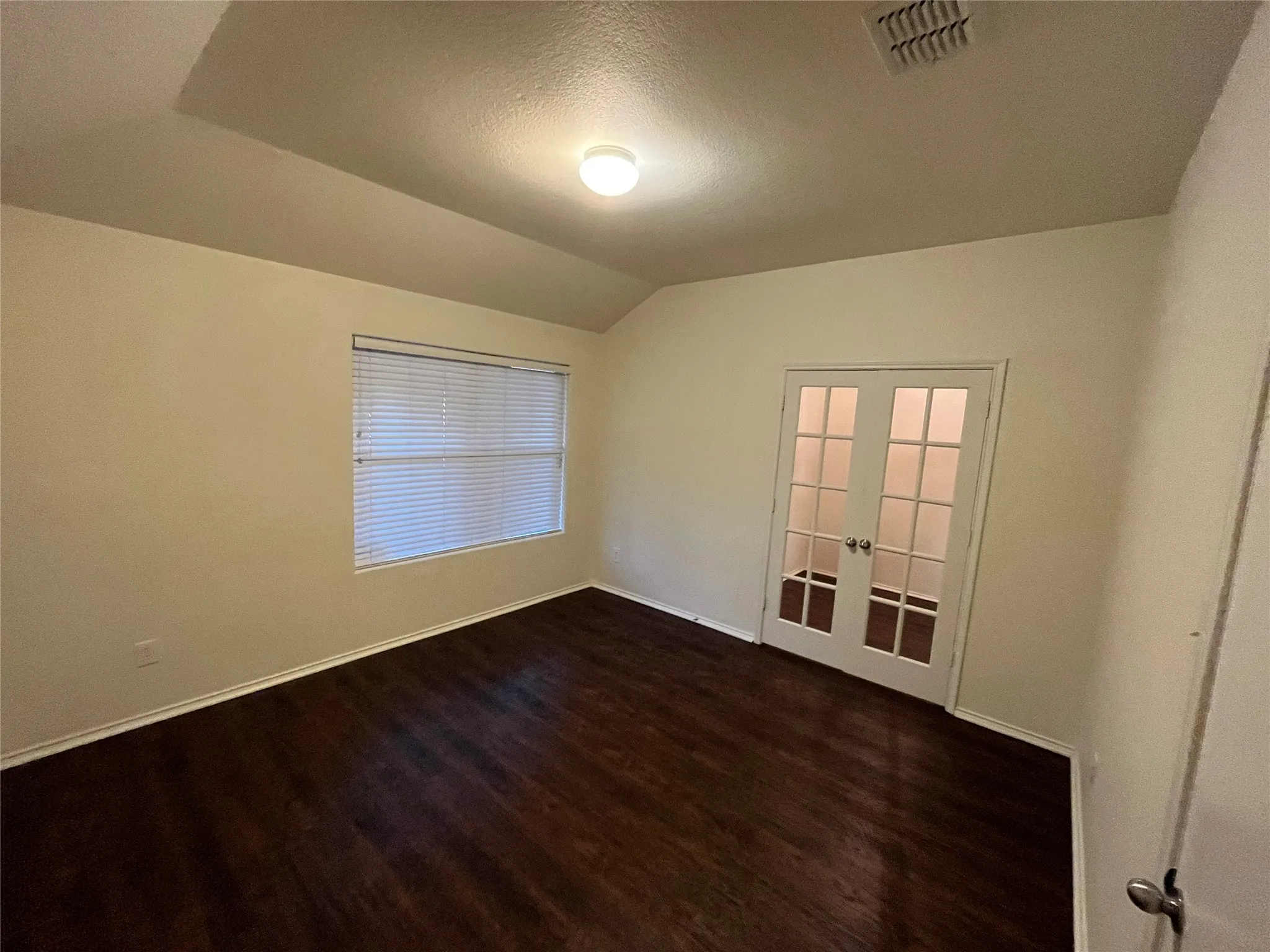 Room featuring dark wood-finish flooring, a window with horizontal blinds, and a tray ceiling