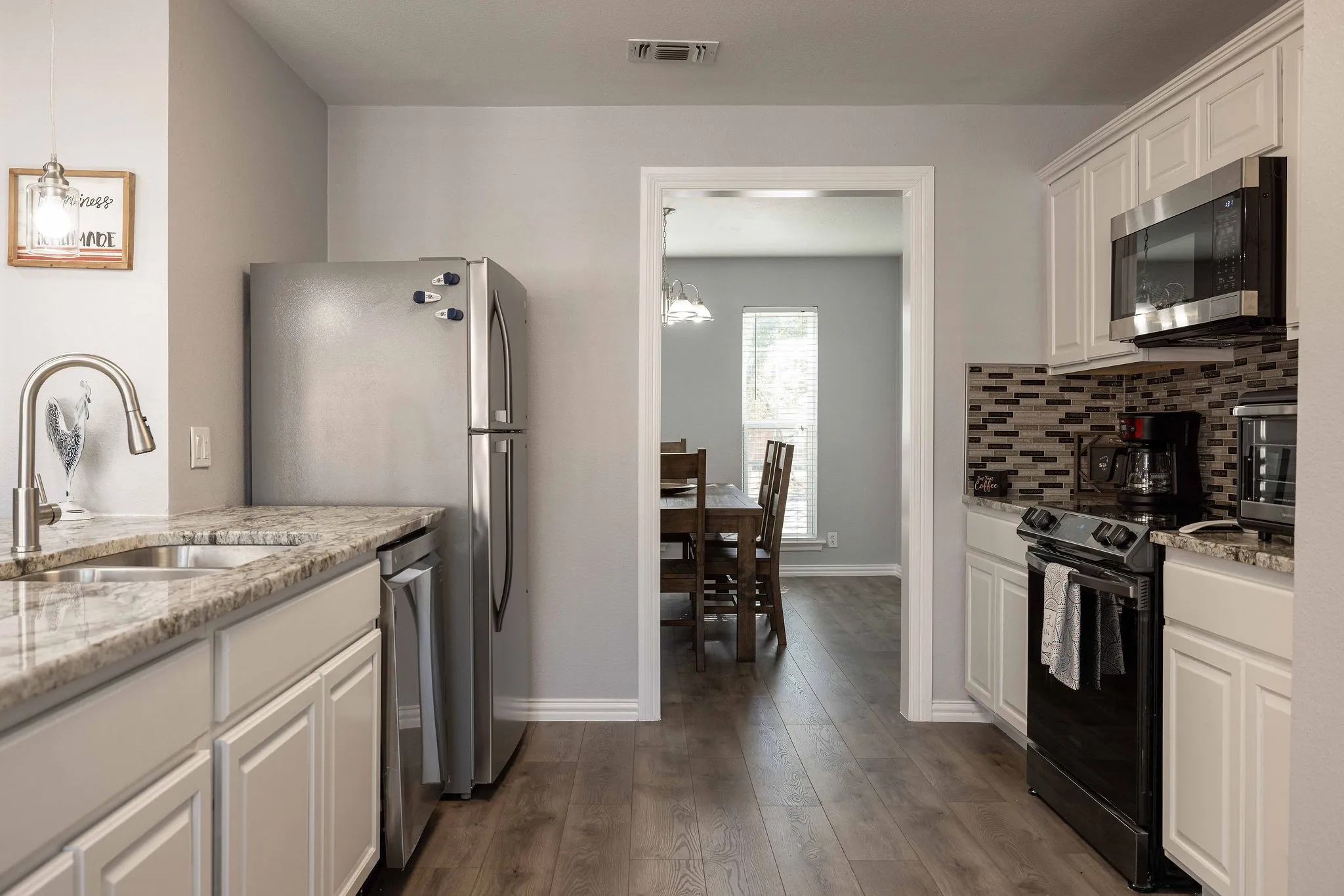 Kitchen featuring stainless steel appliances, a sink, white cabinetry, dark wood finished floors, and baseboards