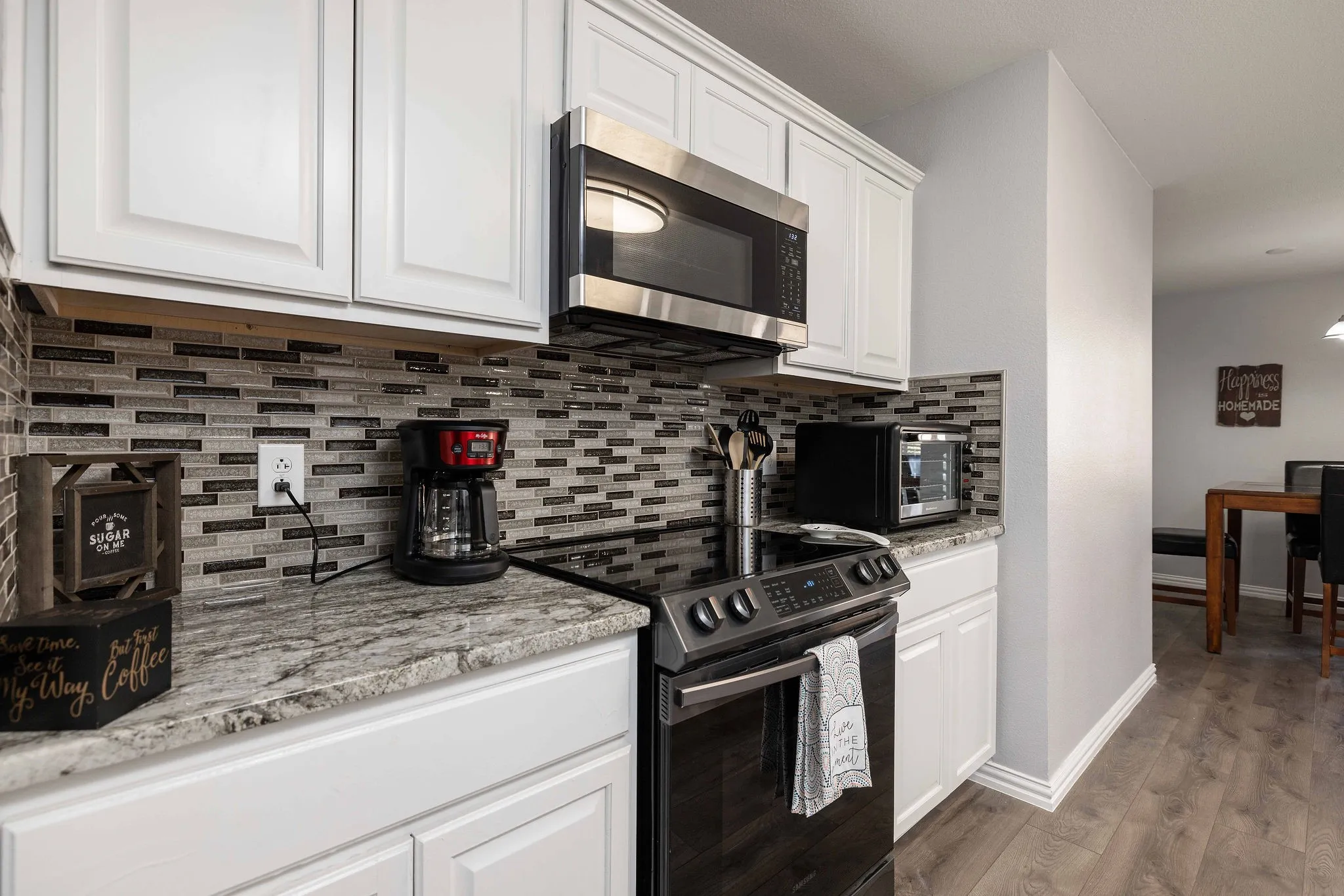 Kitchen featuring stainless steel microwave, electric range oven, backsplash, white cabinetry, and wood finished floors