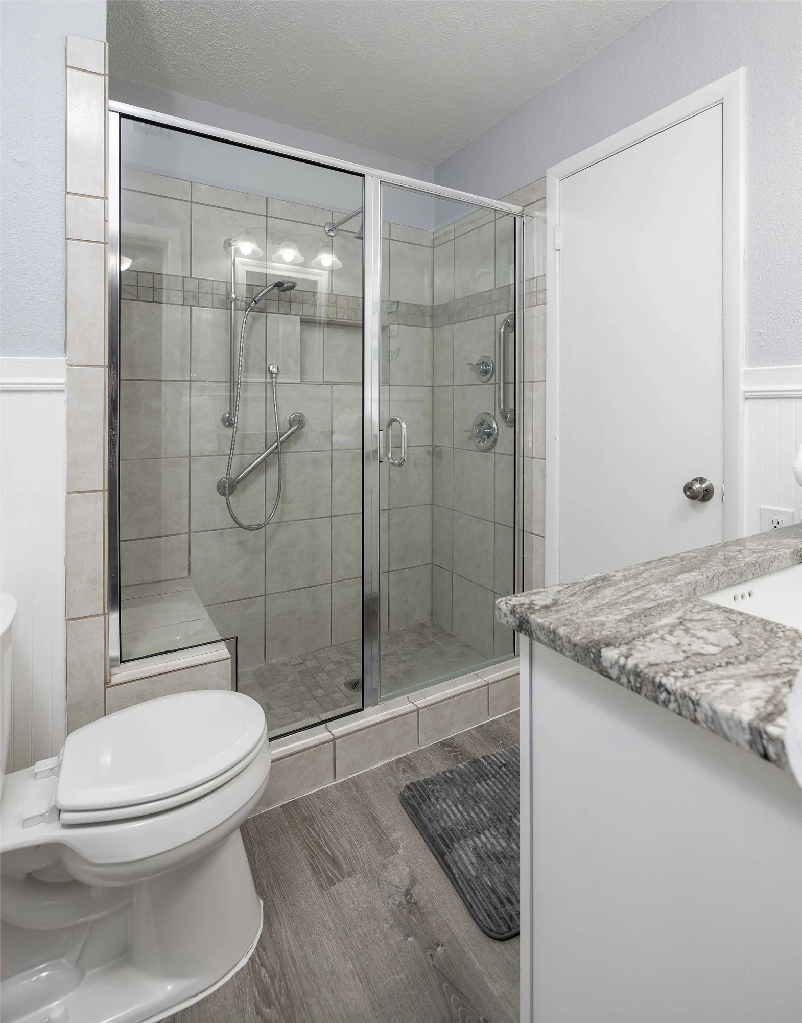 Full bath with toilet, wood finished floors, vanity, a shower stall, and a wainscoted wall