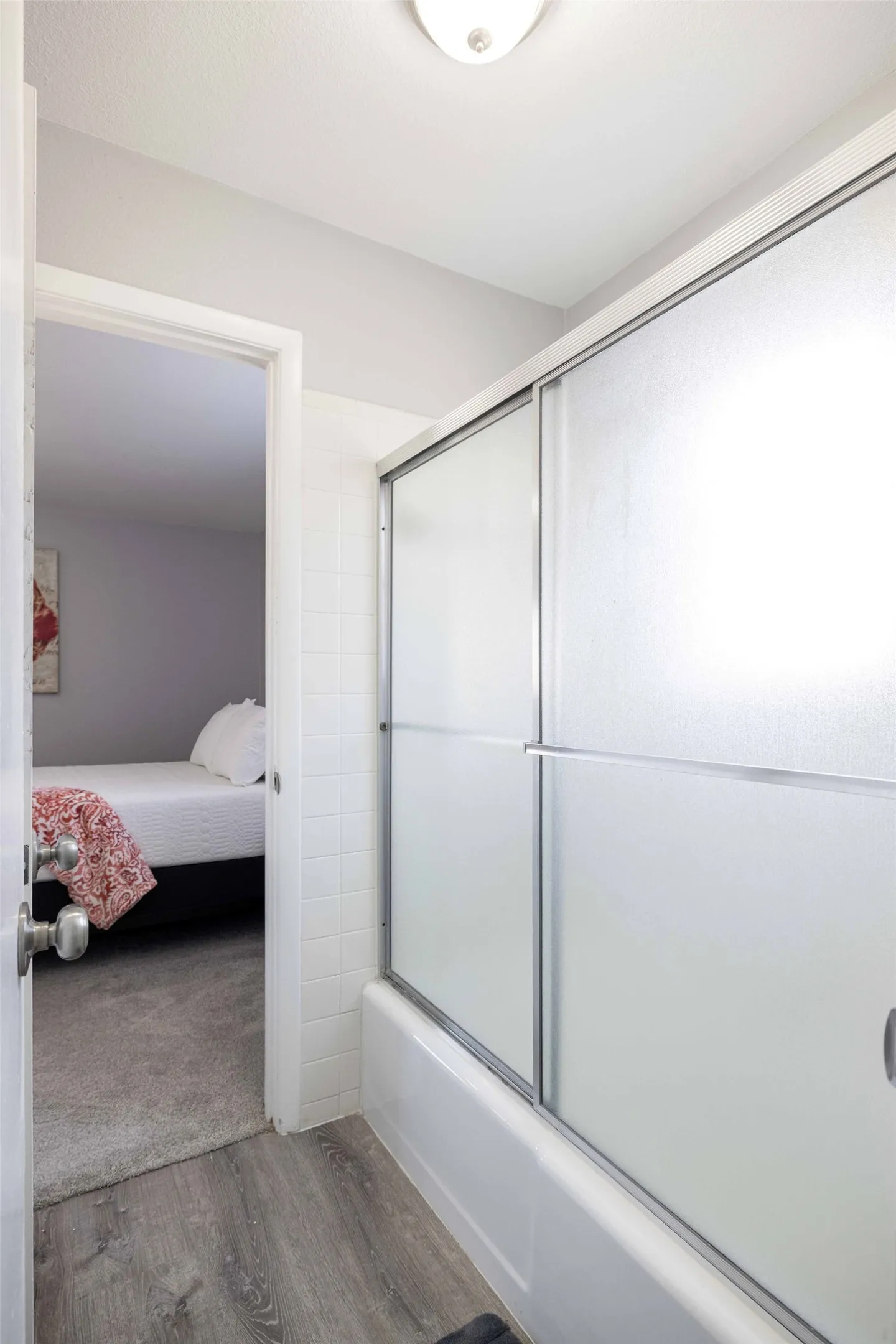 Full bath featuring ensuite bath, wood finished floors, and shower / bath combination with glass door