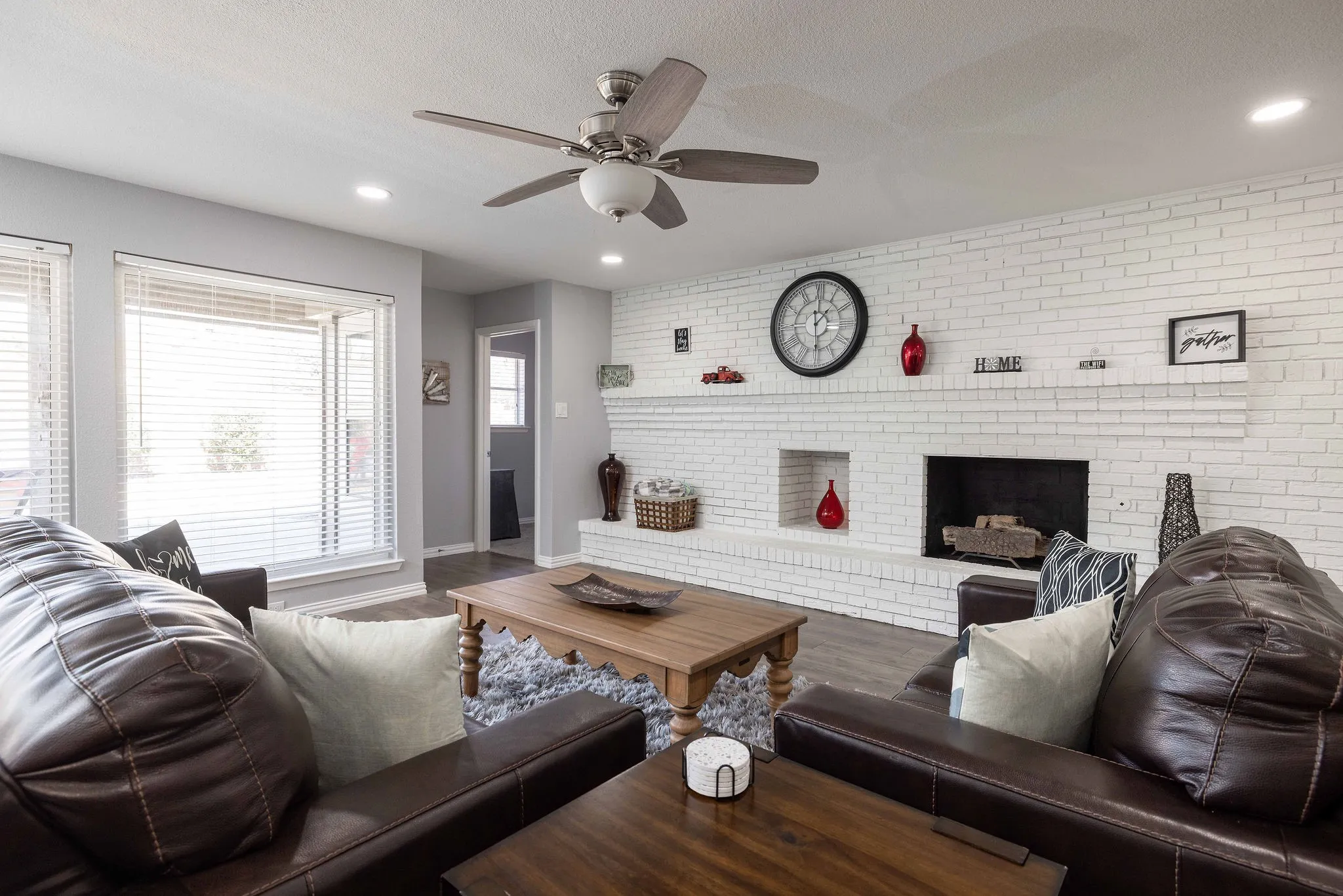 Living area featuring a brick fireplace, a ceiling fan, dark wood-style floors, recessed lighting, and baseboards