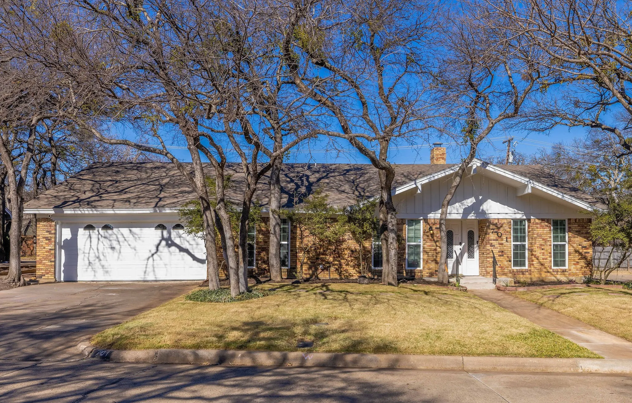 Ranch-style home with brick siding, a chimney, a front yard, asphalt driveway, and an attached garage