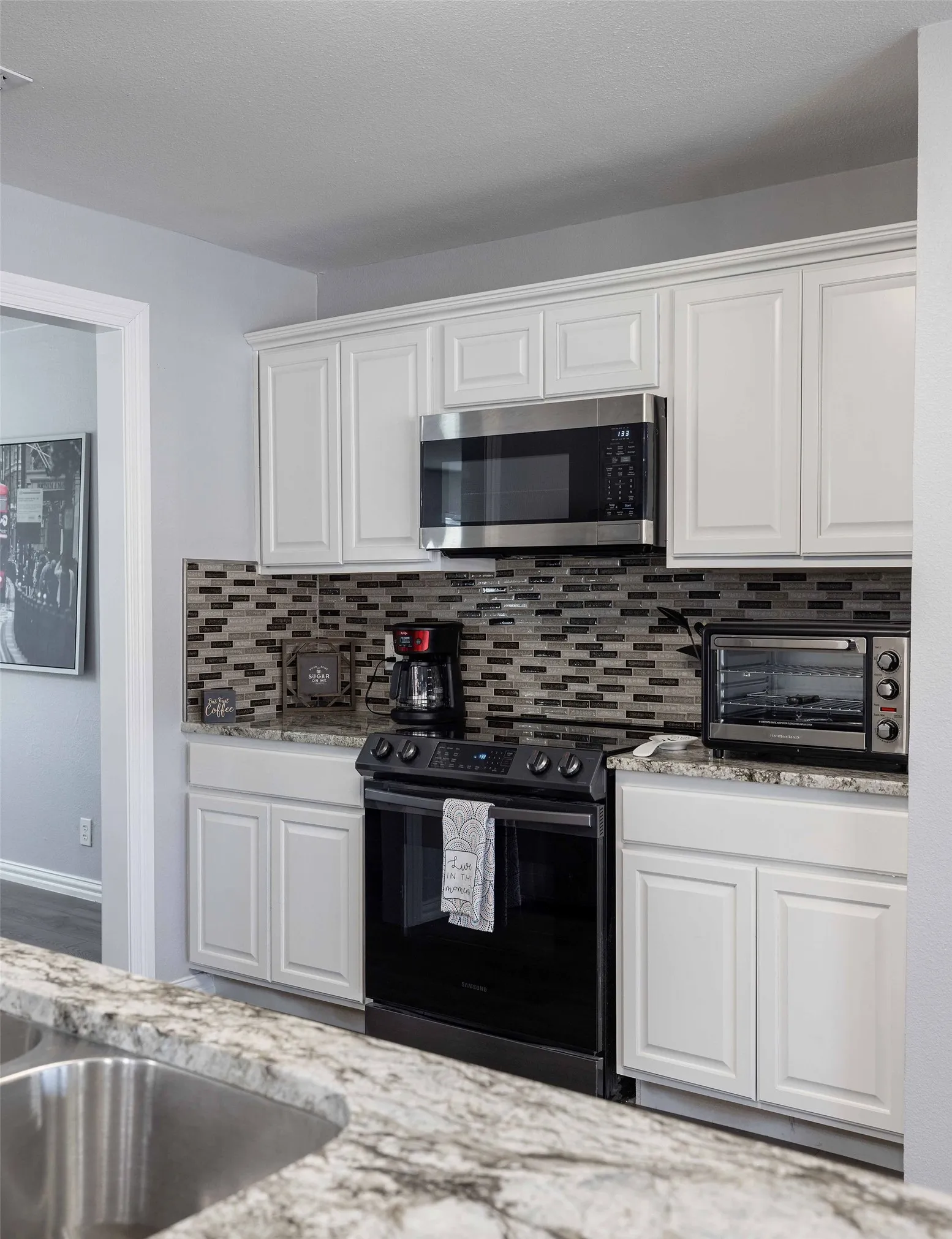 Kitchen featuring stainless steel microwave, black range with electric stovetop, decorative backsplash, white cabinets, and a sink
