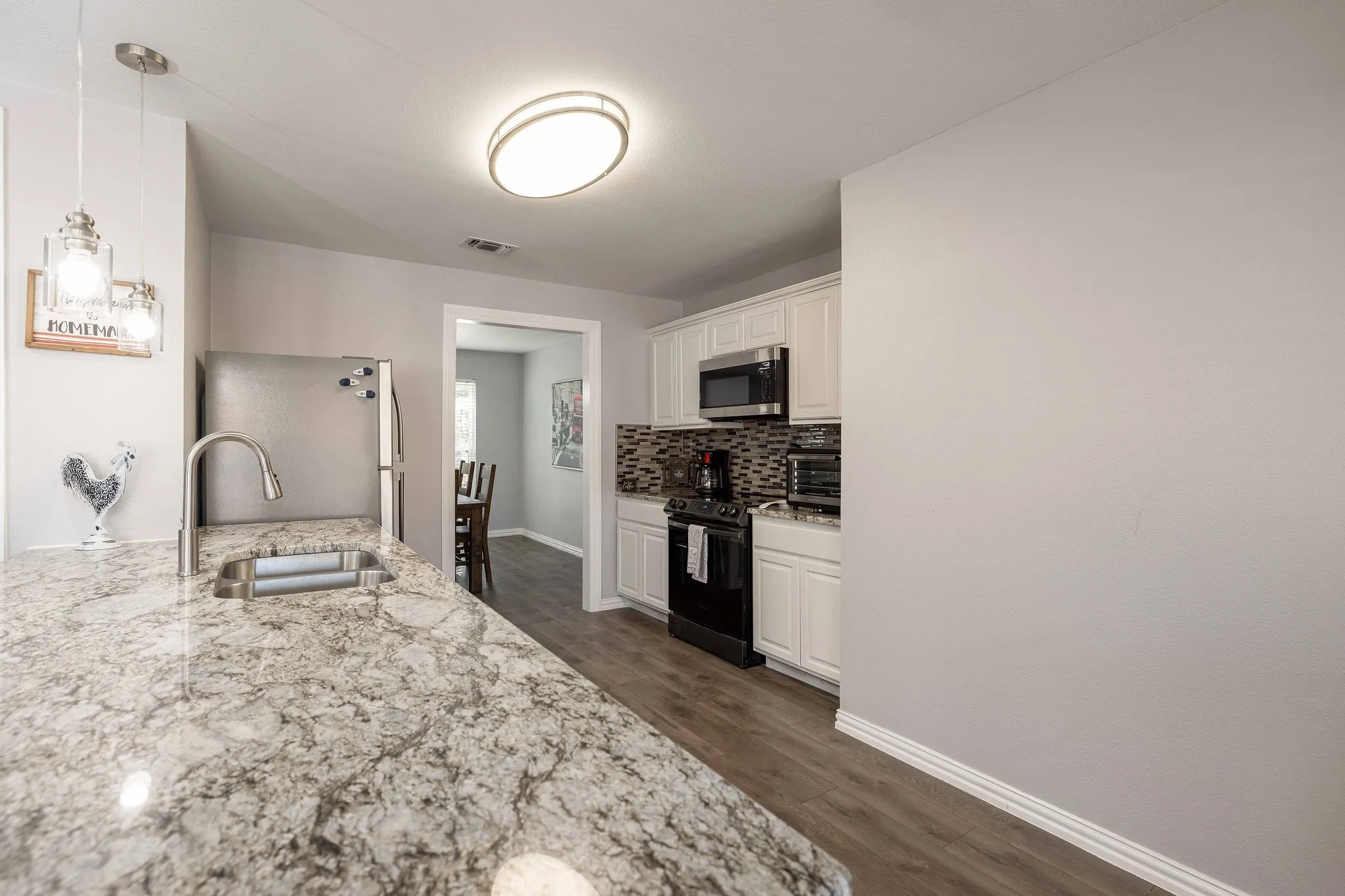 Kitchen featuring stainless steel microwave, freestanding refrigerator, black range with electric cooktop, a sink, and decorative backsplash