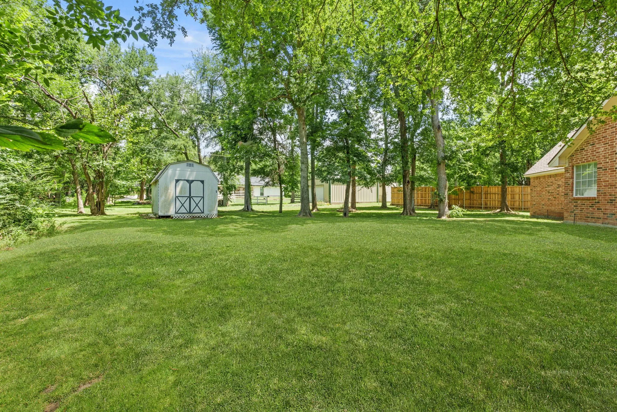 Outdoors, enjoy a covered front porch, extended back patio shaded by mature trees, sprinkler system, storage building, fire pit, and a side-yard garden area framed with landscape timbers.