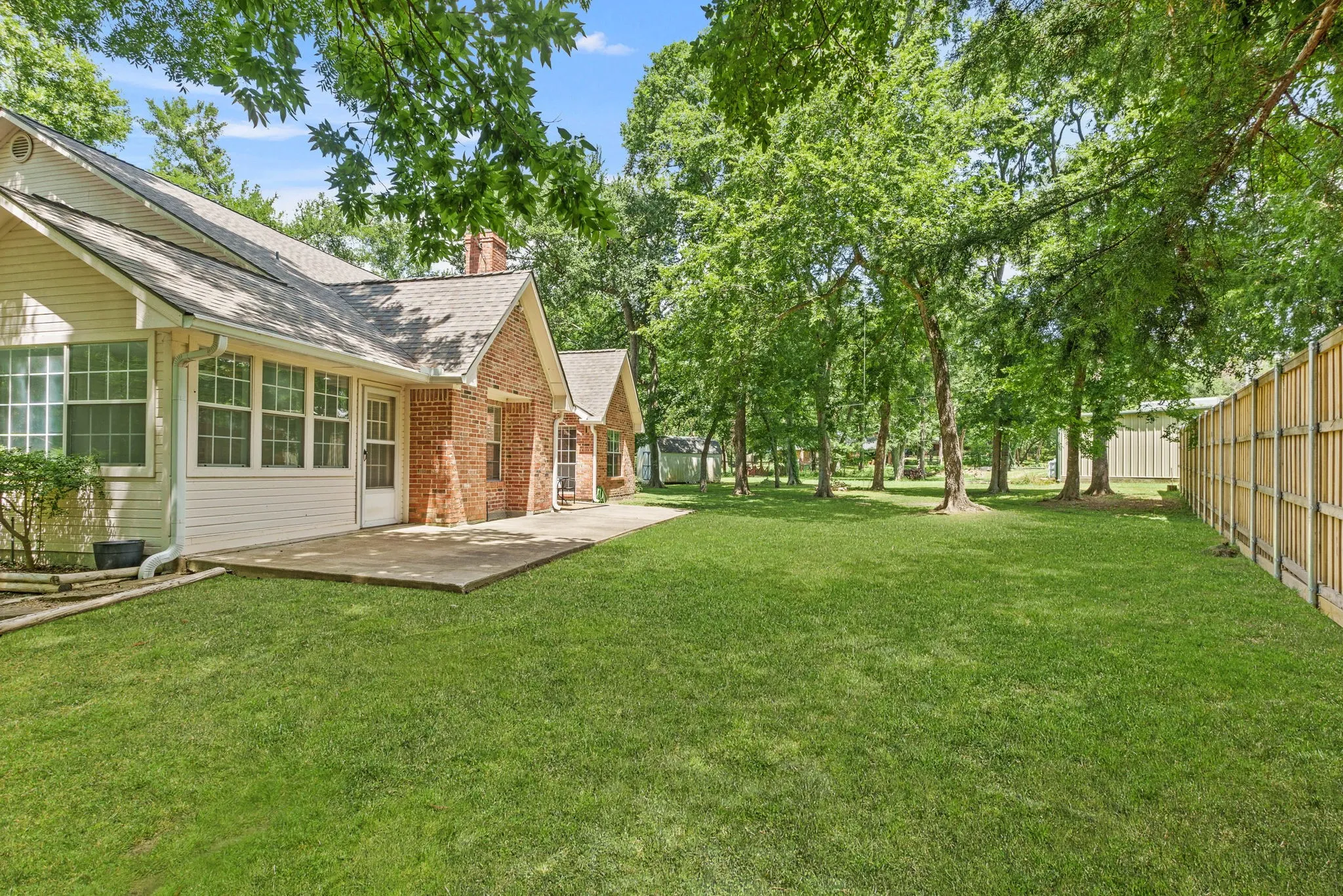 Outdoors, enjoy a covered front porch, extended back patio shaded by mature trees, sprinkler system, storage building, fire pit, and a side-yard garden area framed with landscape timbers.