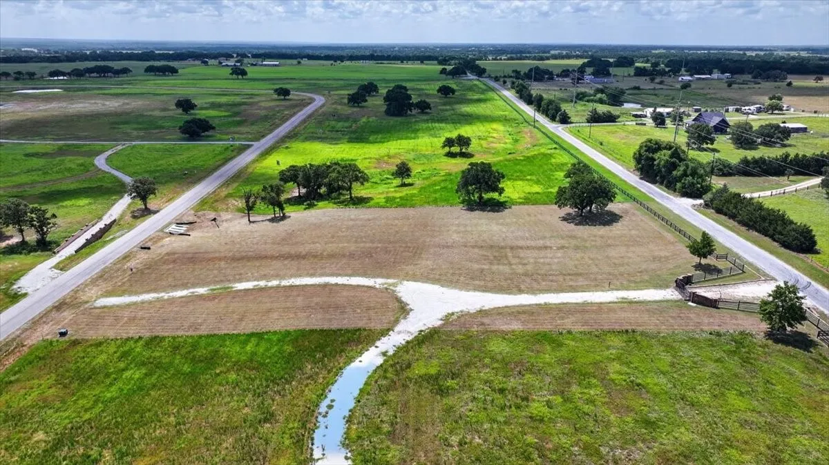 Expansive rural property featuring a long gravel driveway, a small water feature, mature trees, and frontage on two paved roads