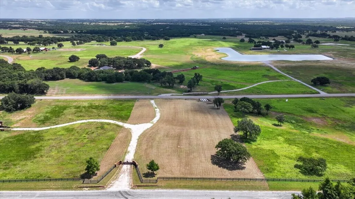 Expansive acreage featuring a private gated entrance, established access roads, scattered mature trees, and a distant pond
