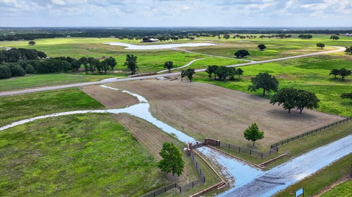 Expansive undeveloped land featuring a stone-columned entry gate, perimeter fencing, mature trees, and a winding gravel road