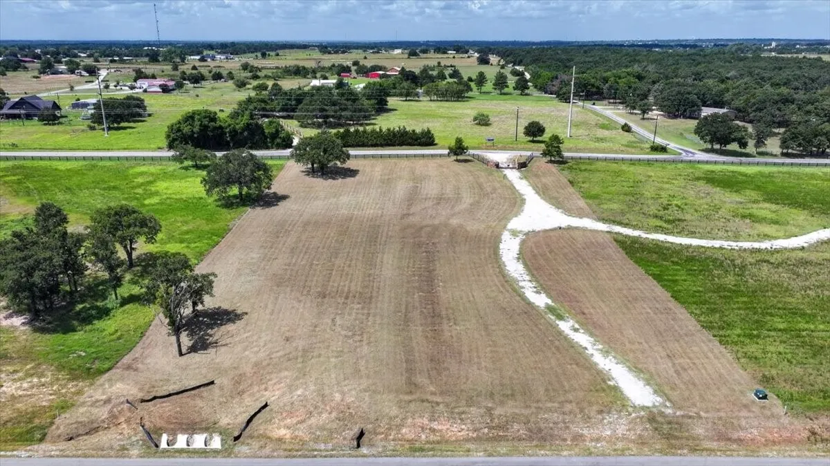 Expansive cleared land parcel featuring a gravel driveway and mature trees