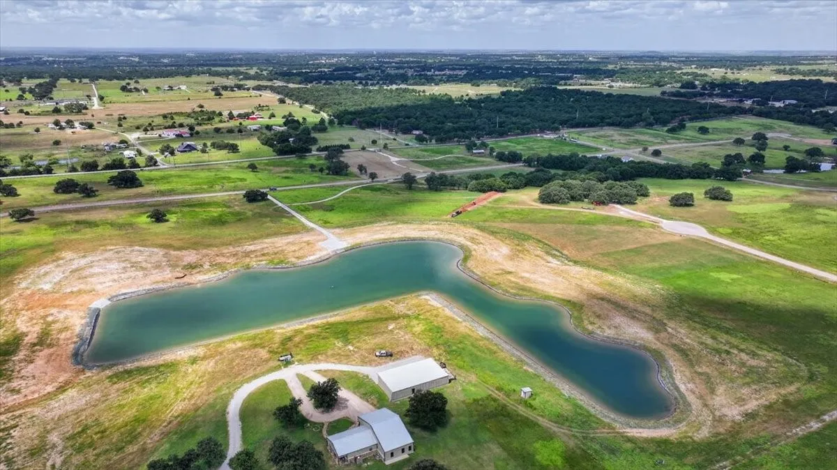 Expansive acreage featuring a private body of water, multiple outbuildings, and a gravel drive