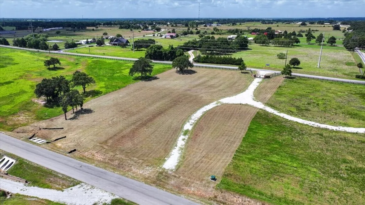 Expansive property featuring a cleared building site, mature trees, partial fencing, and a gravel driveway system