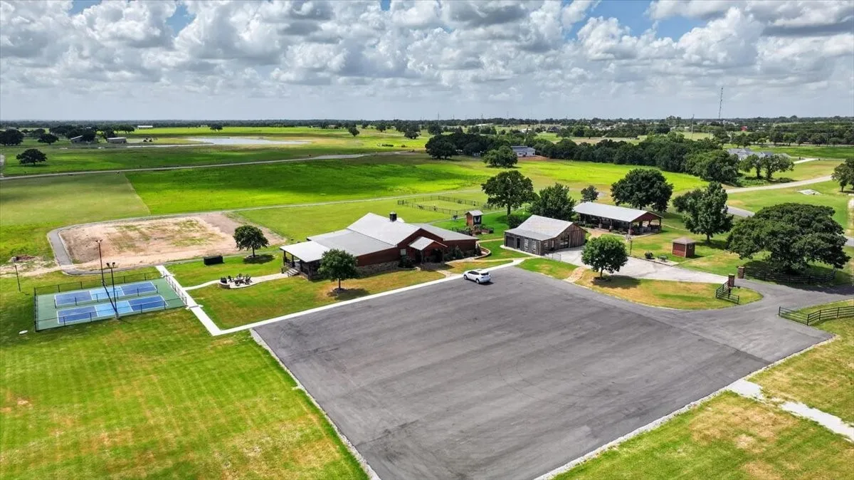 Expansive property featuring multiple buildings with metal roofs, a large paved parking area, two outdoor courts, and abundant green space with scattered trees