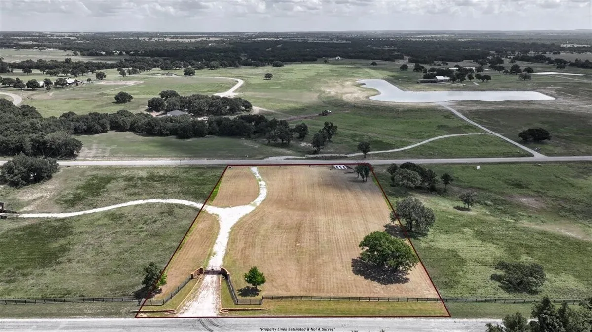 Expansive open lot featuring a paved entrance, established trees, and surrounding green acreage