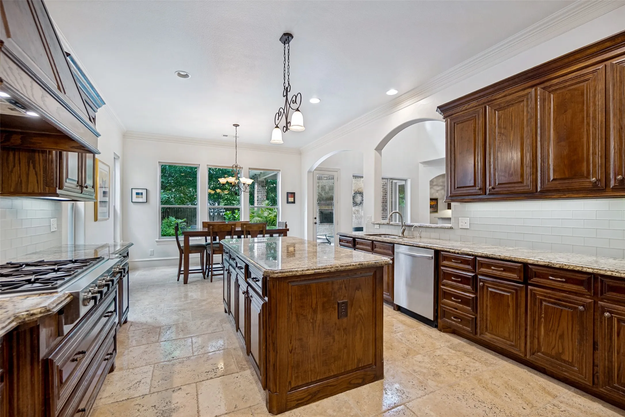 Gourmet kitchen with rich wood cabinetry, stone countertops, stainless steel appliances, a center island, and natural tile flooring