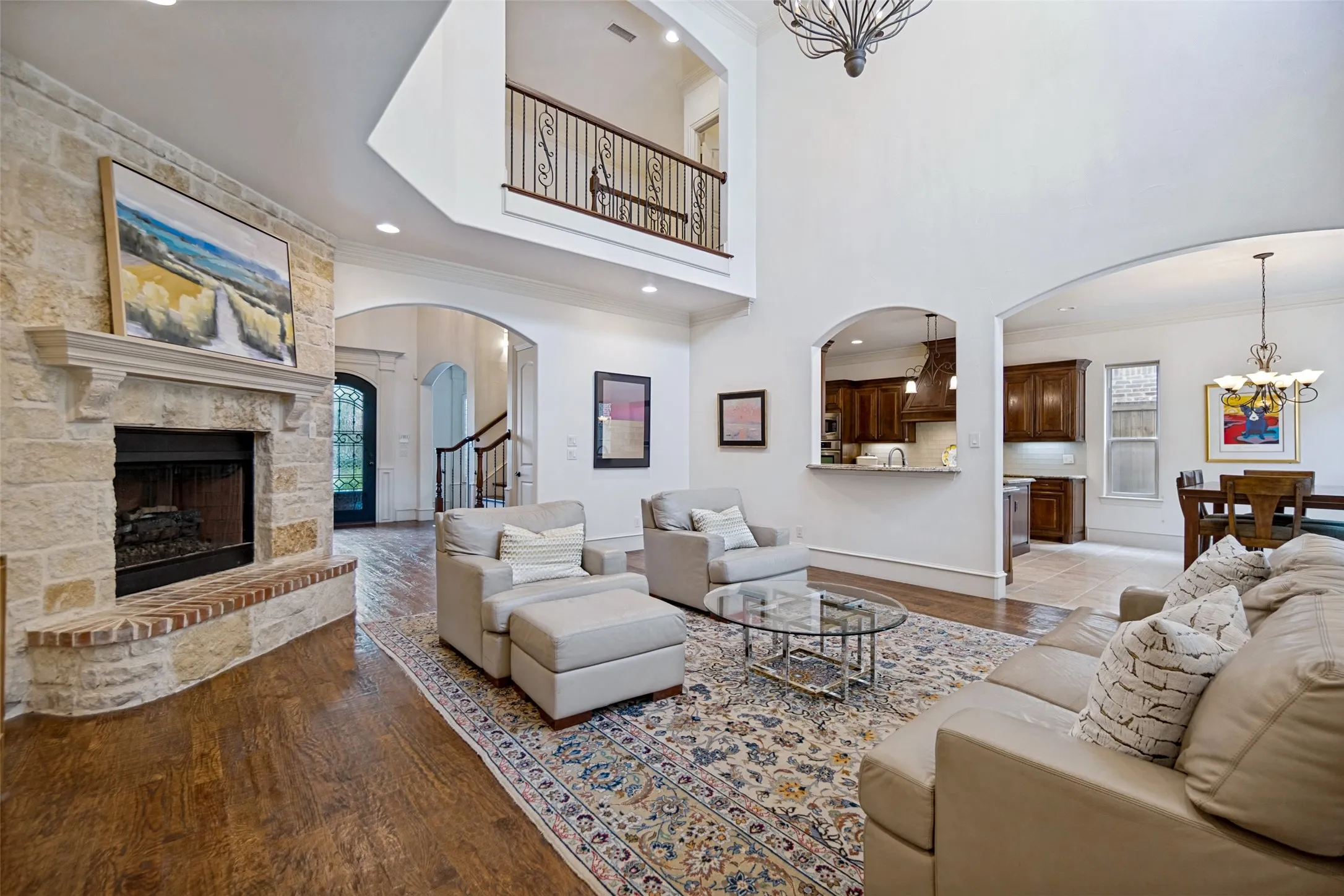 Living area featuring a stone fireplace with a wood mantle, wood-finish flooring, and a second-story balcony with an ornate iron railing
